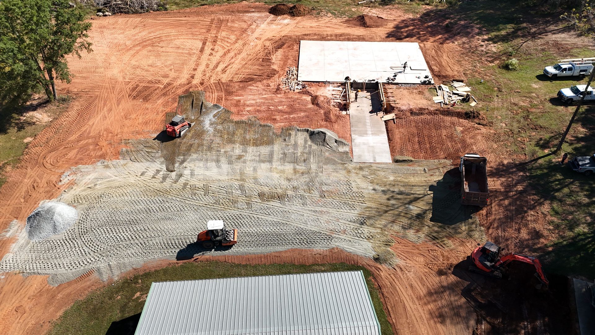 Aerial view of construction site with machinery and gravel path leading to building.