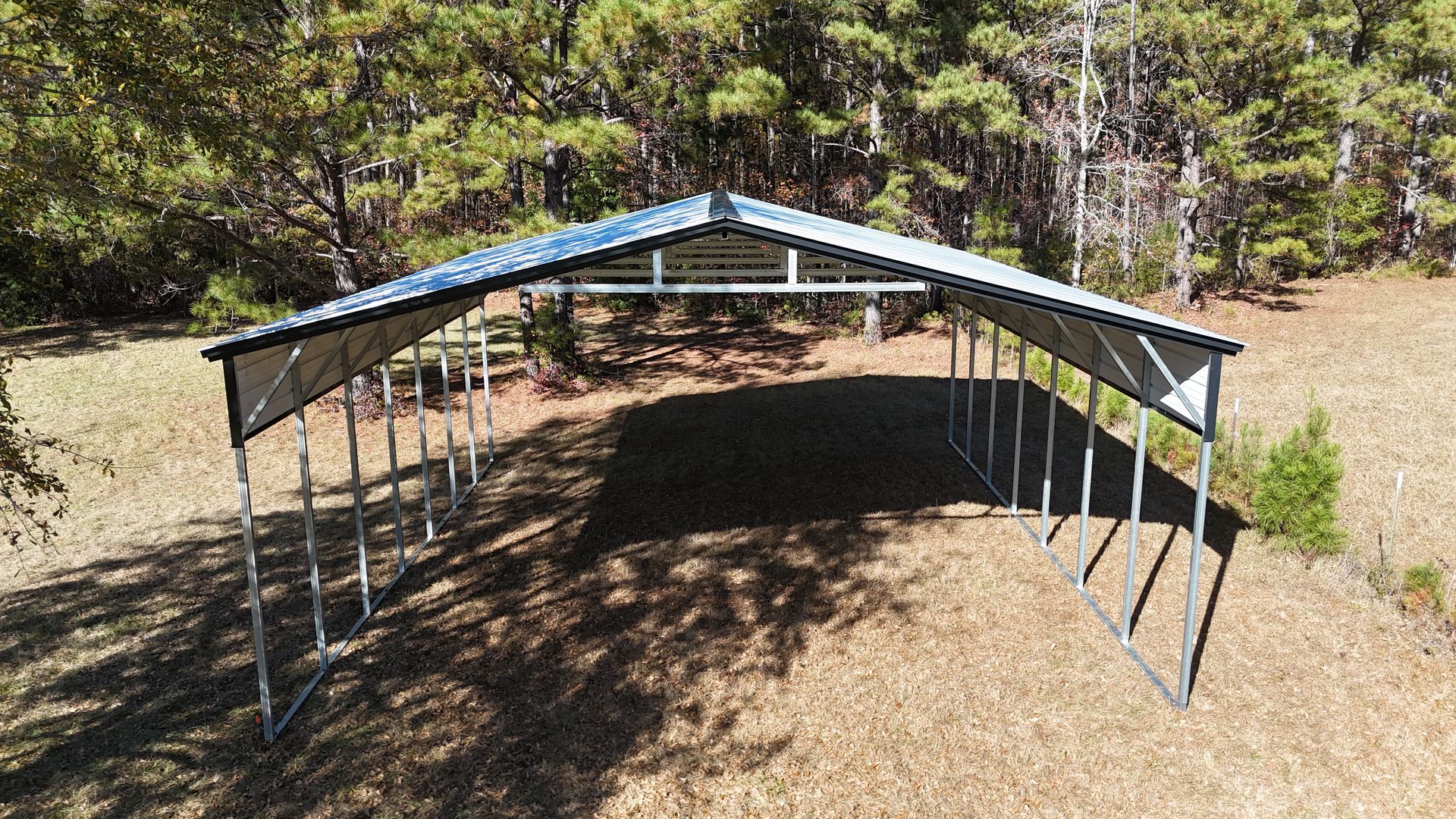 Metal carport in a field, surrounded by trees.