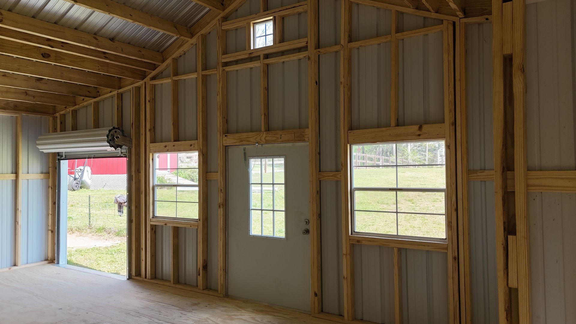 Interior of an unfinished metal building with a white entry door, two windows, and a roll-up garage door.