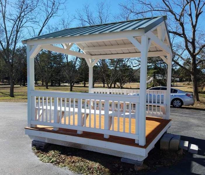 A white gazebo with a green roof sits in a parking lot