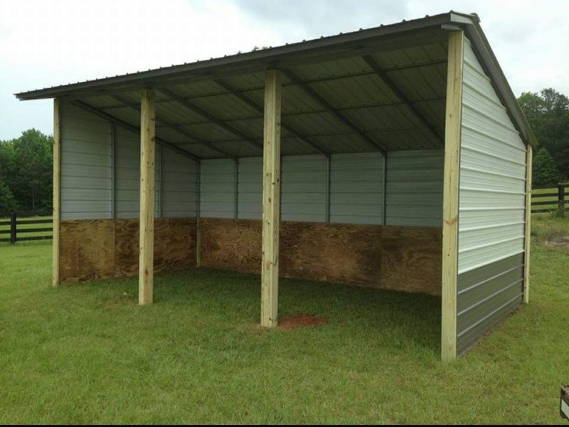 A shed with a roof and wooden posts in a grassy field