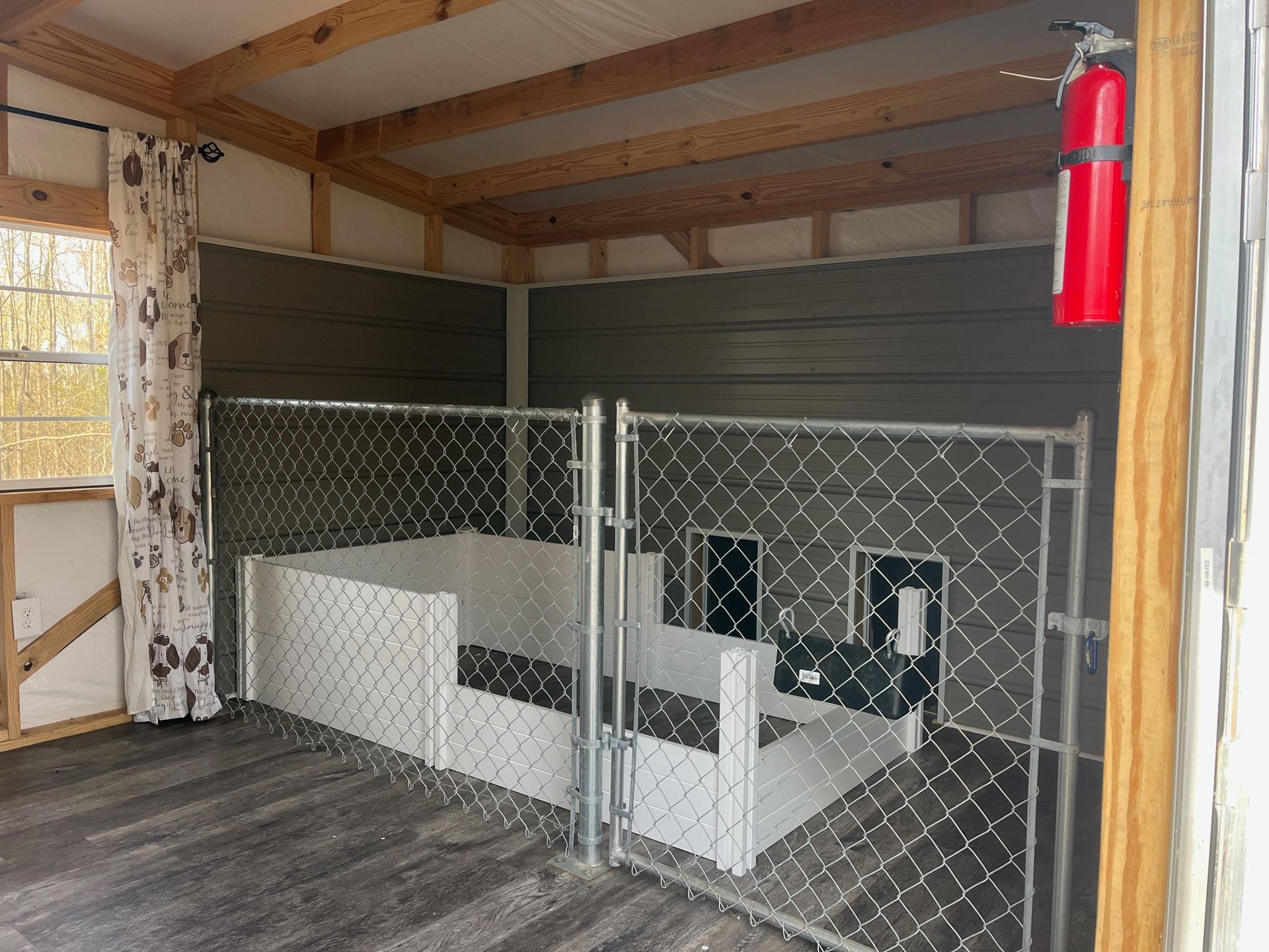 Dog kennel interior with two gated areas, a white dog bed, and a red fire extinguisher.