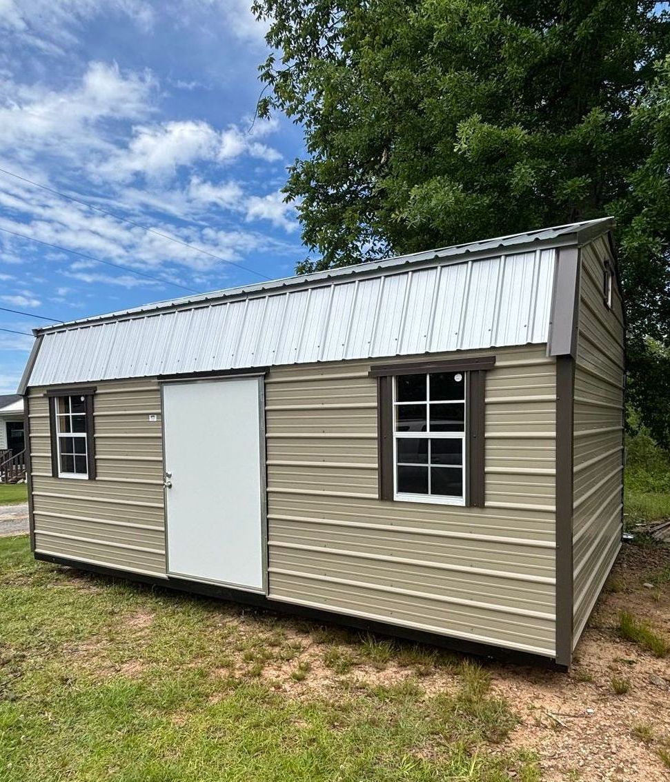 A small metal shed with a white door and windows is sitting in the middle of a grassy field.