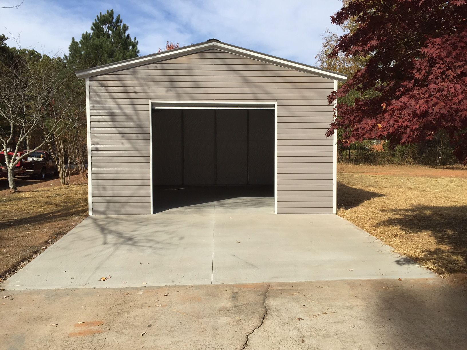 Gray metal garage with open door, on a concrete slab in a yard.