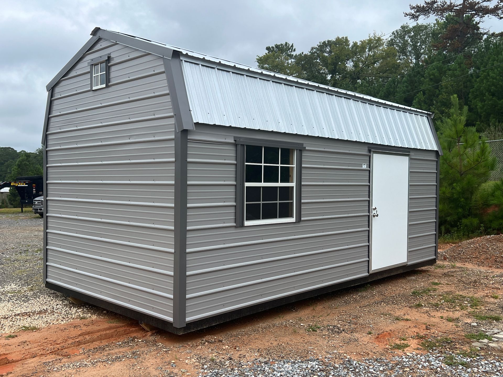 A small shed with a window and a door is sitting in the middle of a dirt field.