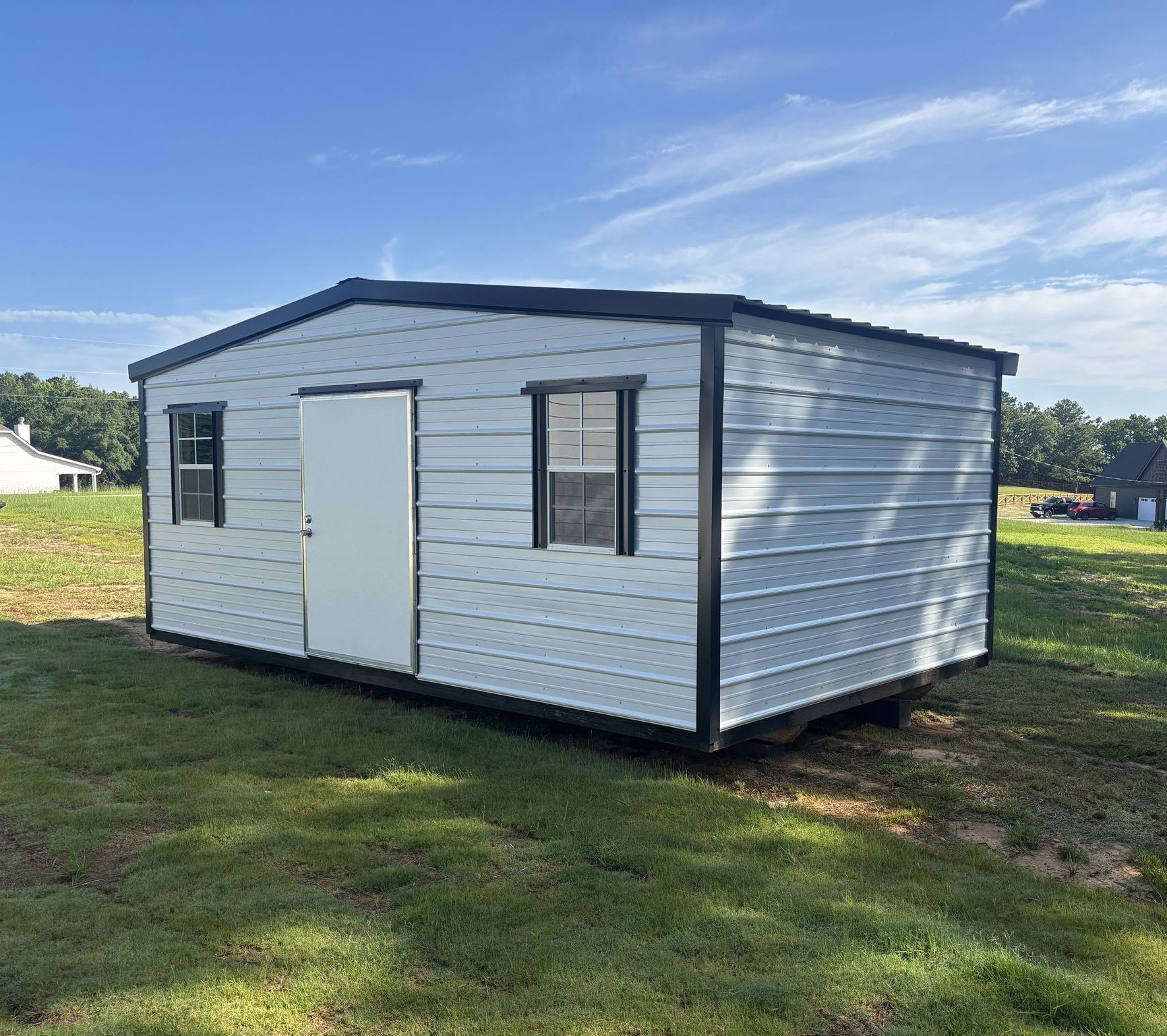 A small white shed is sitting in the middle of a grassy field.