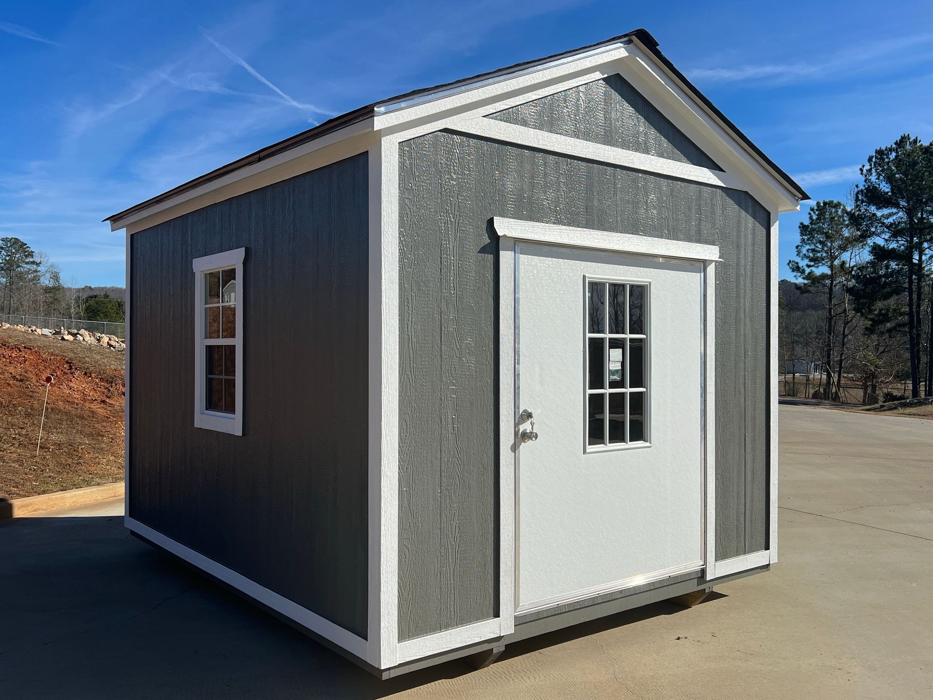 Gray storage shed with white trim, door, and window; blue sky background.