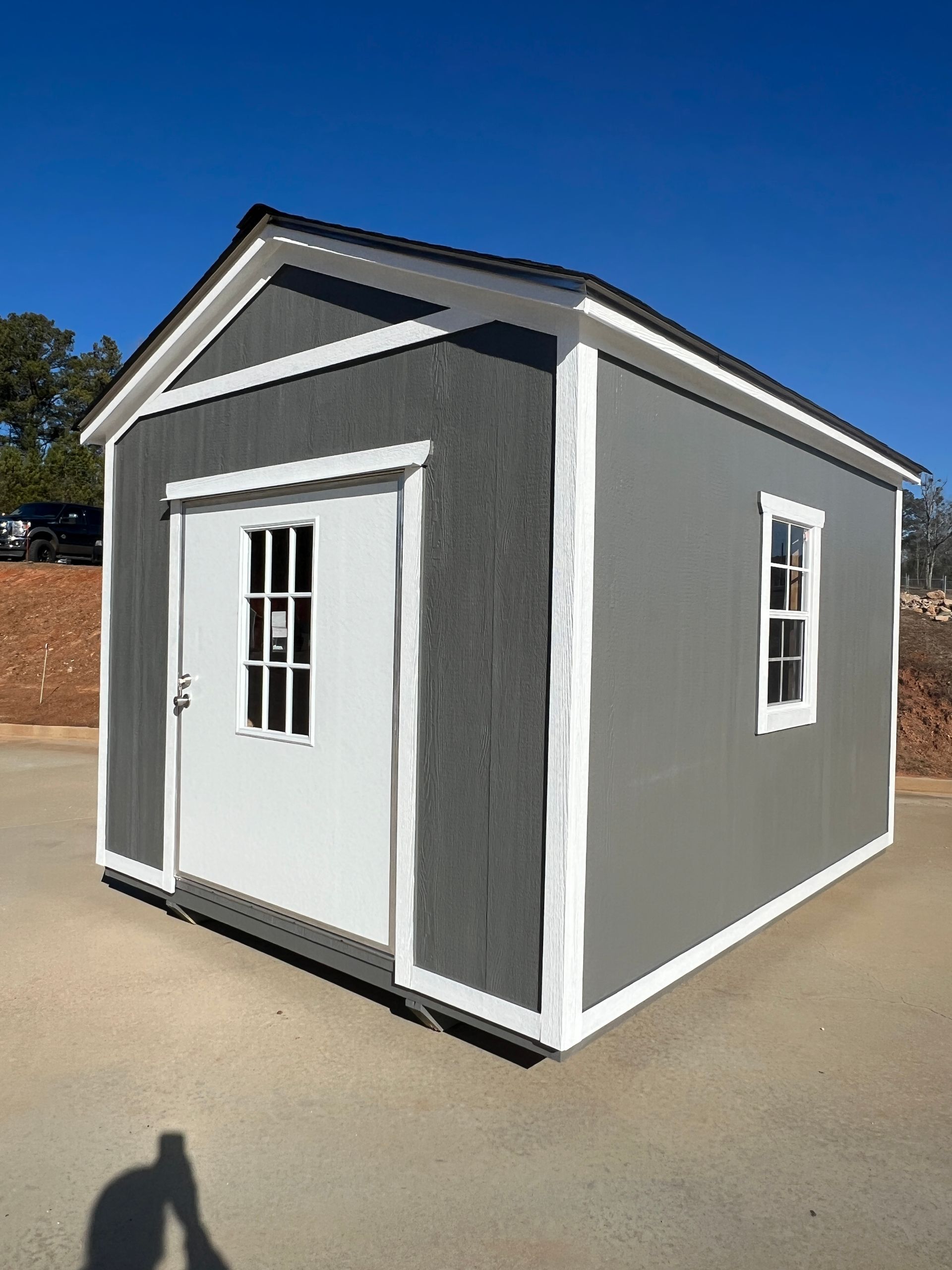 Gray shed with white trim, door, and window; set against a blue sky.