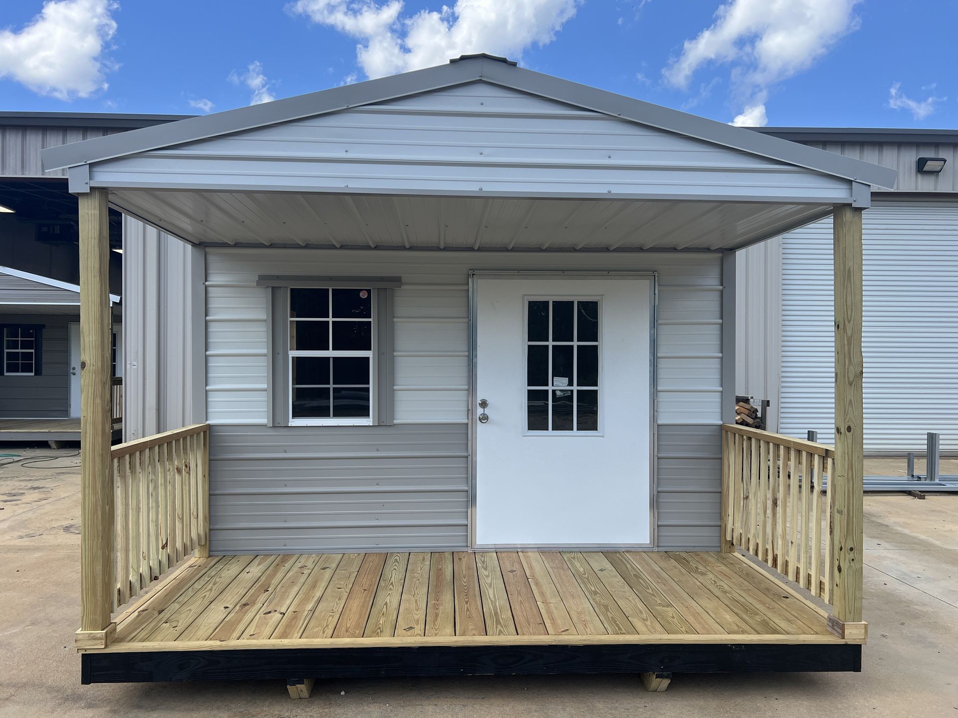 Small grey and white shed with porch and wooden railing on a sunny day.