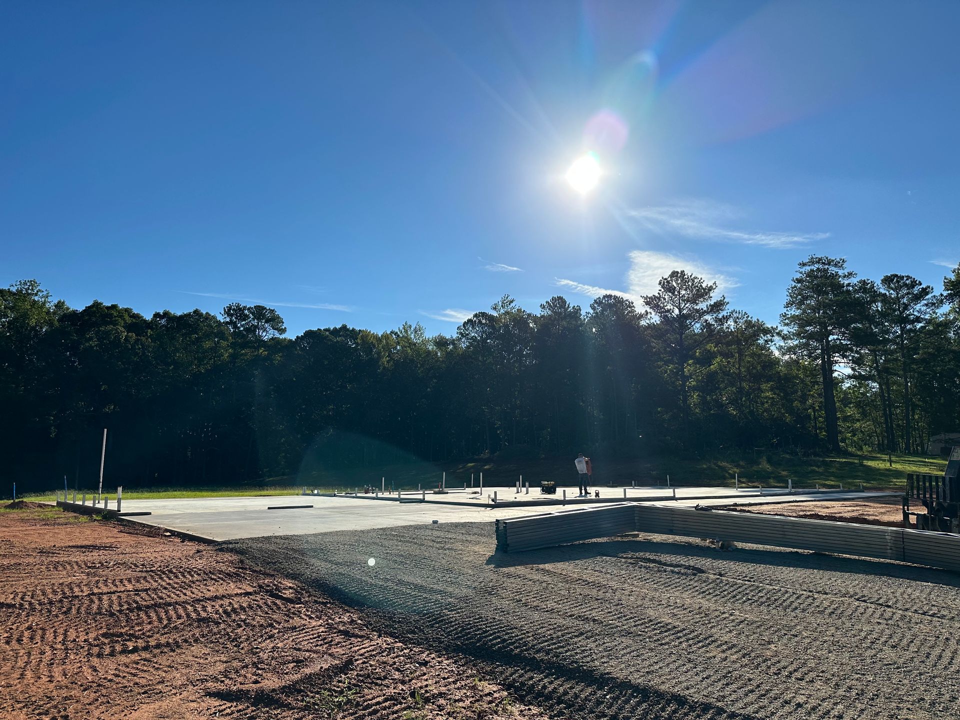 The sun is shining brightly over a dirt field with trees in the background.