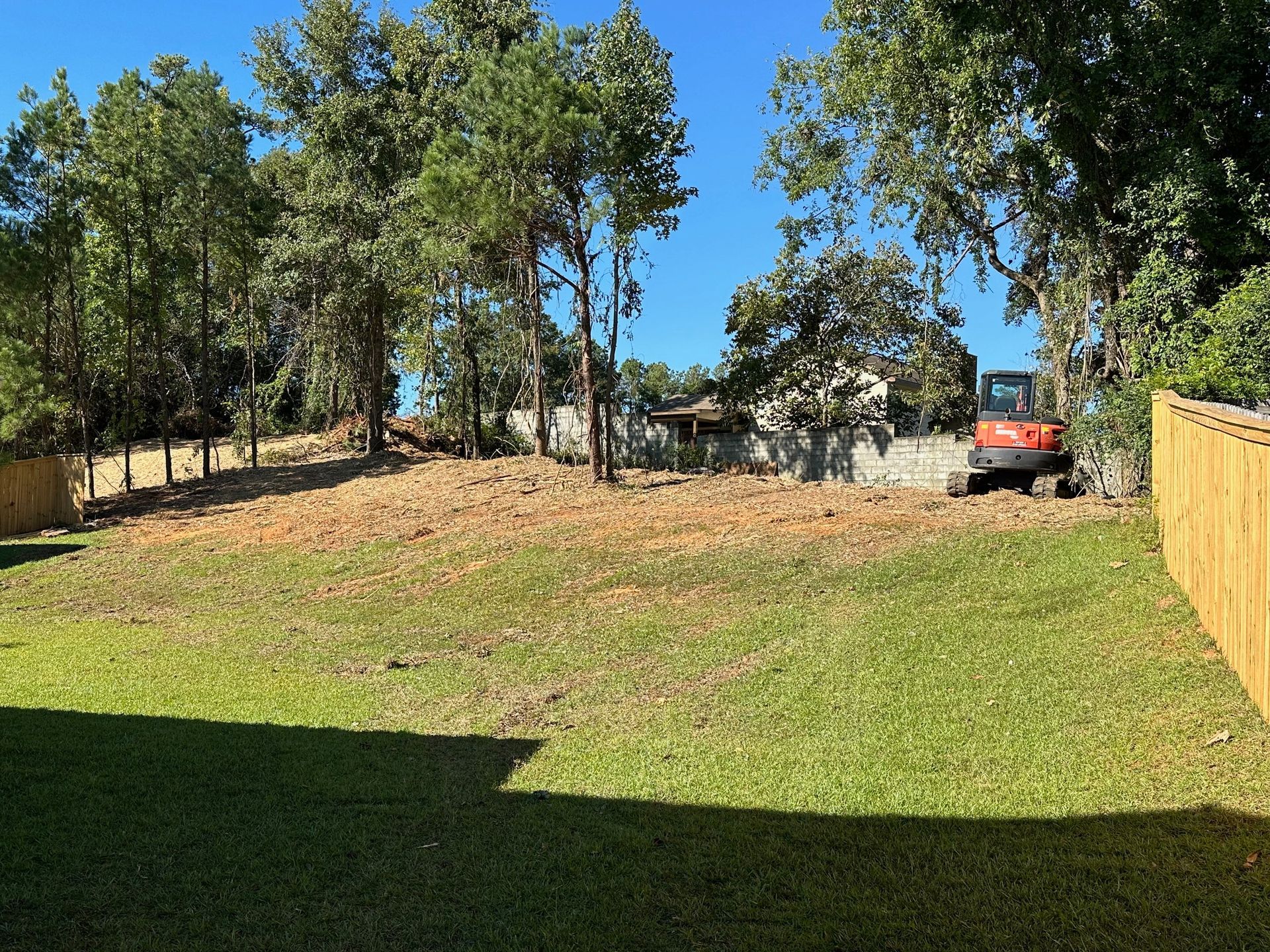 A large lawn with a wooden fence and trees in the background.