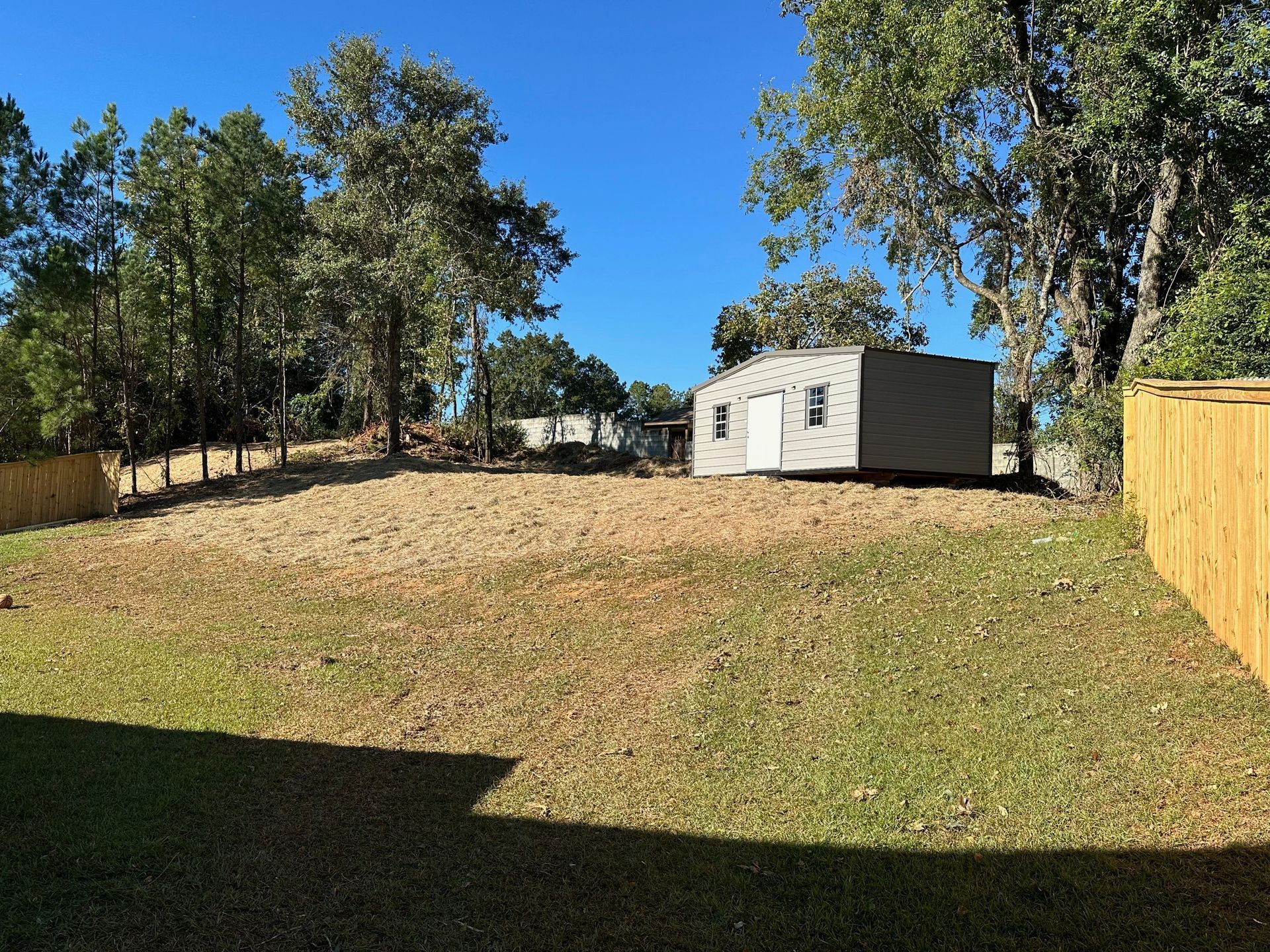 A small house is sitting in the middle of a grassy field next to a wooden fence.