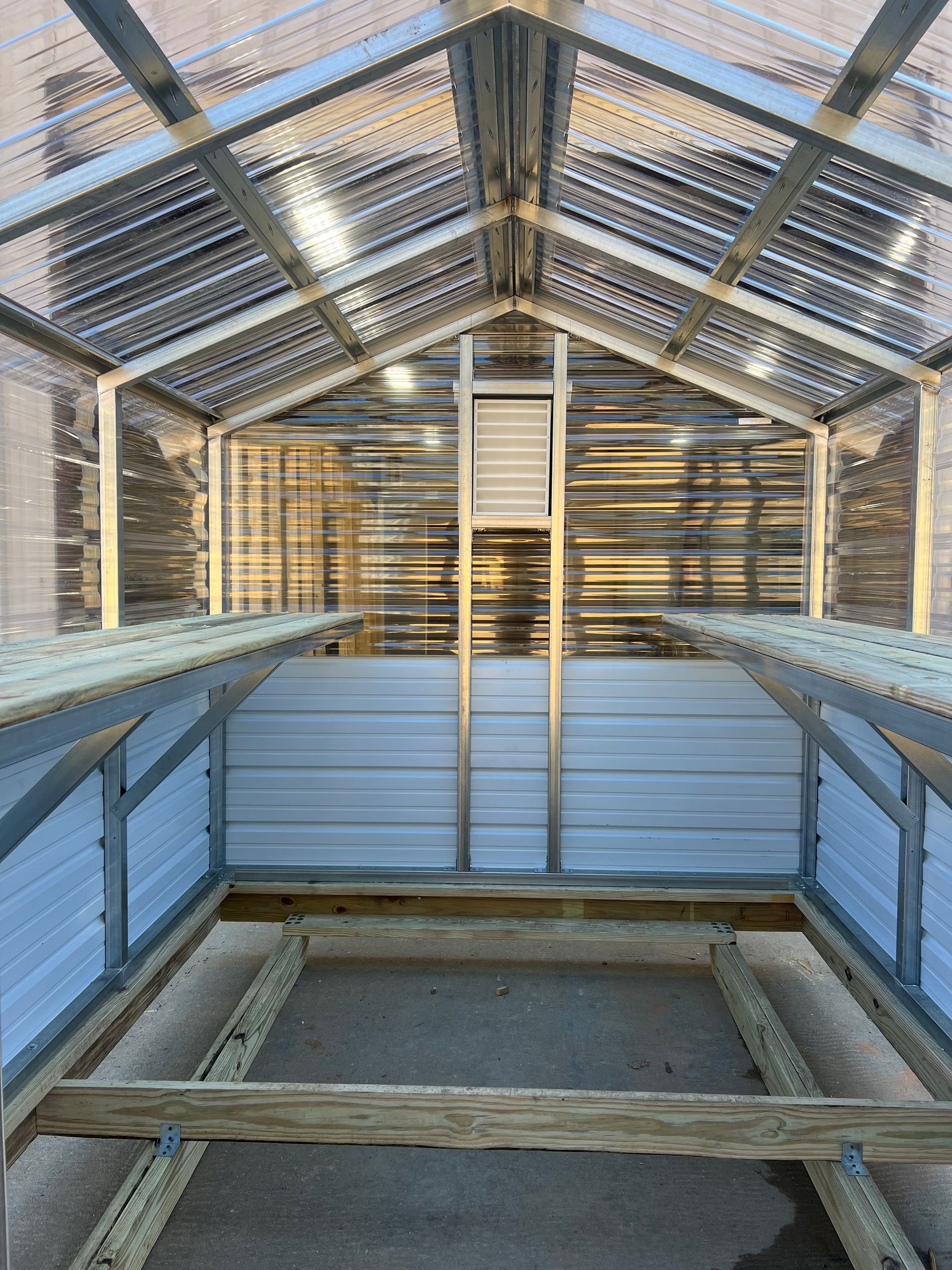 Interior view of an empty greenhouse, with shelving and translucent walls and roof.