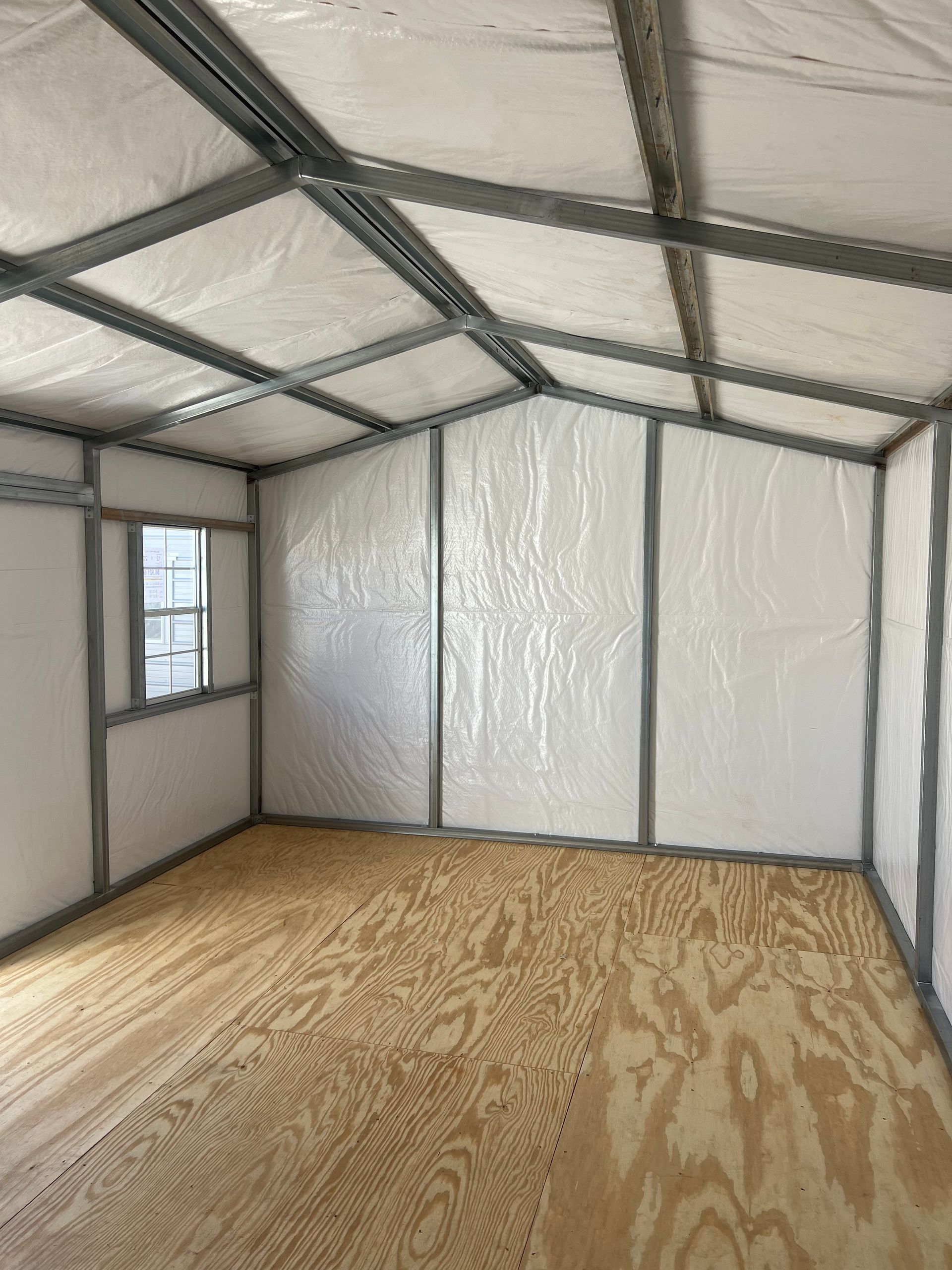 Interior of a small, empty shed with a plywood floor, metal frame, and white walls and ceiling.