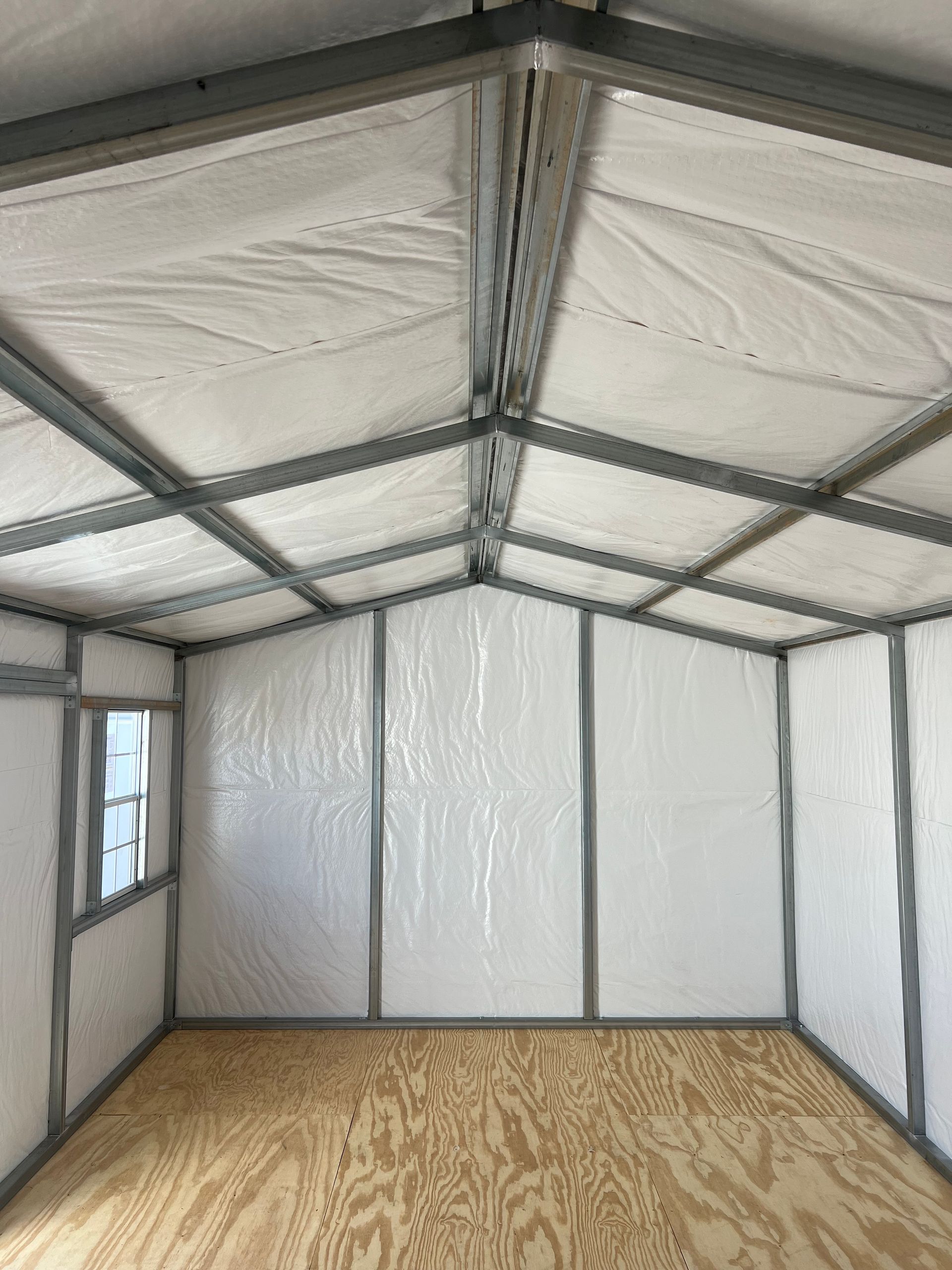 Interior of a metal frame shed with white walls, a wooden floor, and a small window.