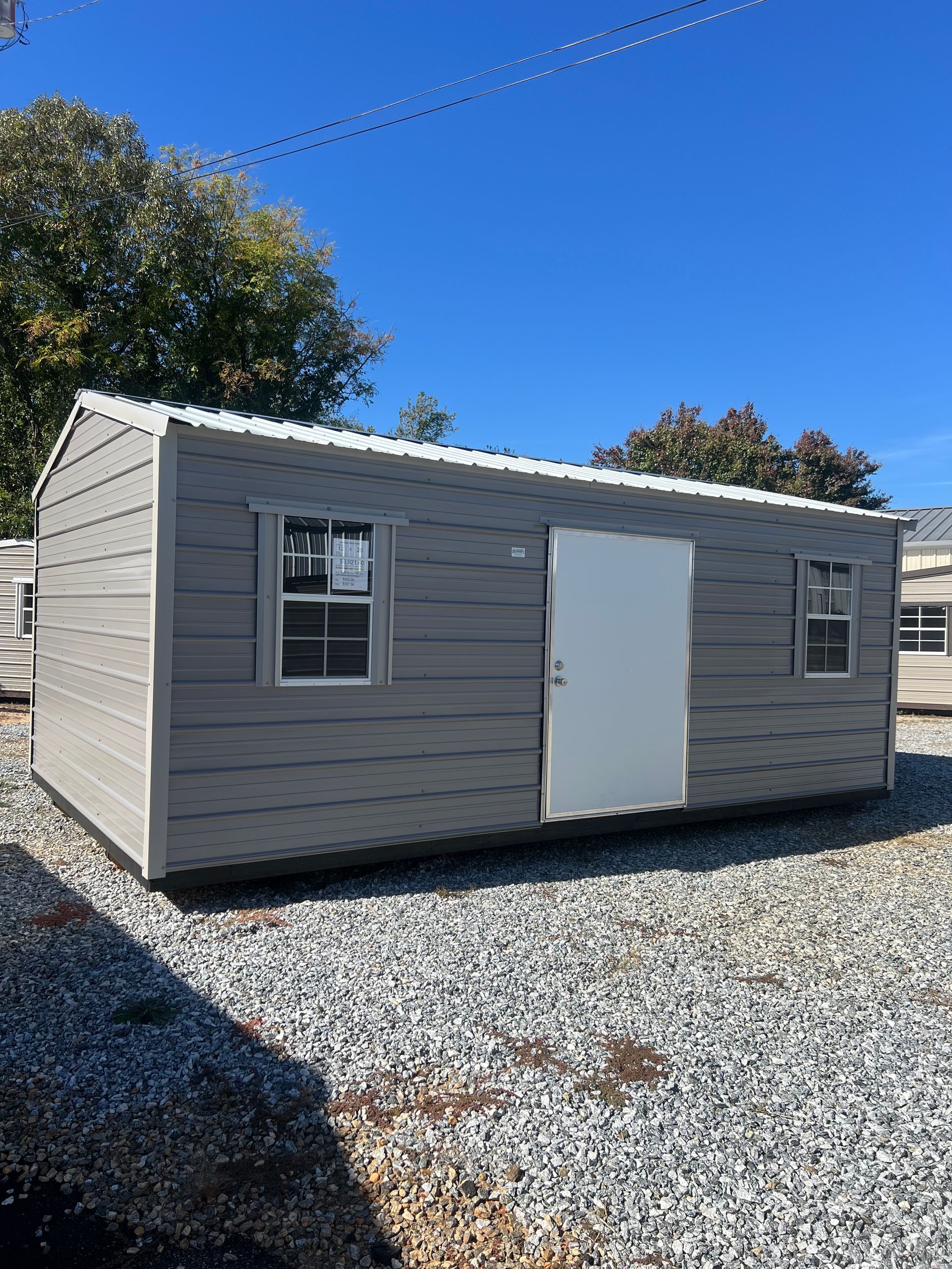 Gray storage shed with white door and windows under a blue sky.