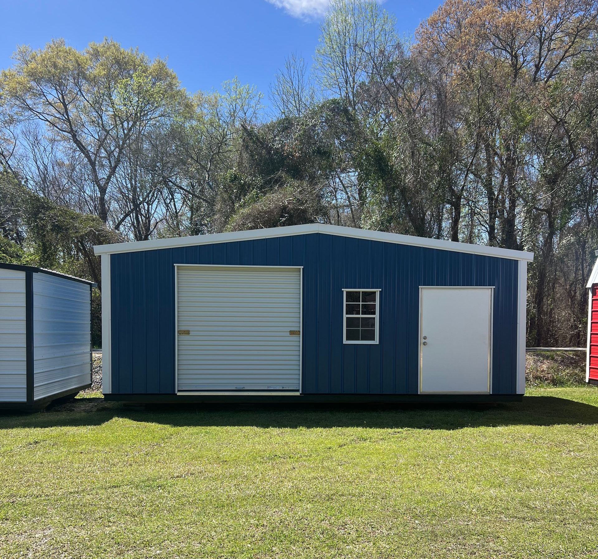 A blue rectangular storage shed with a roll-up garage door, a single white door, and a window, set in a grassy yard.