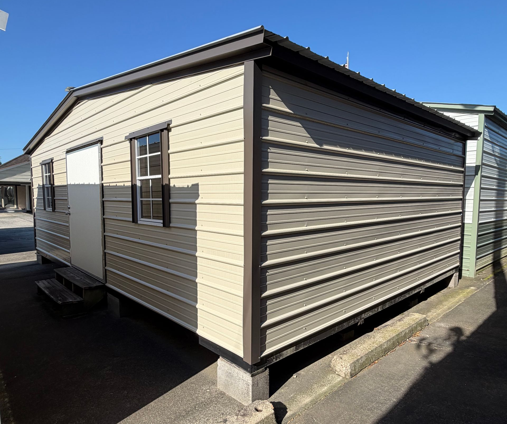 A white metal shed with a garage door is sitting in the middle of a field.