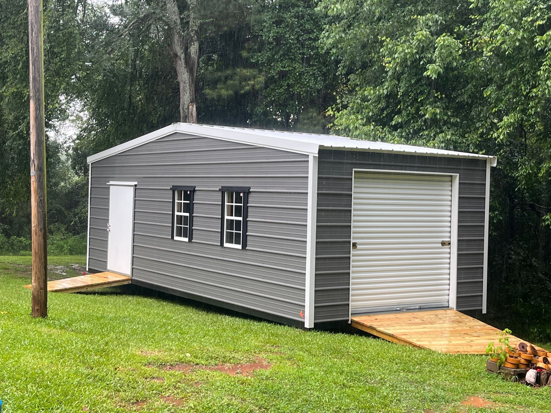 A gray metal garage with a white door and windows is sitting on top of a lush green field.