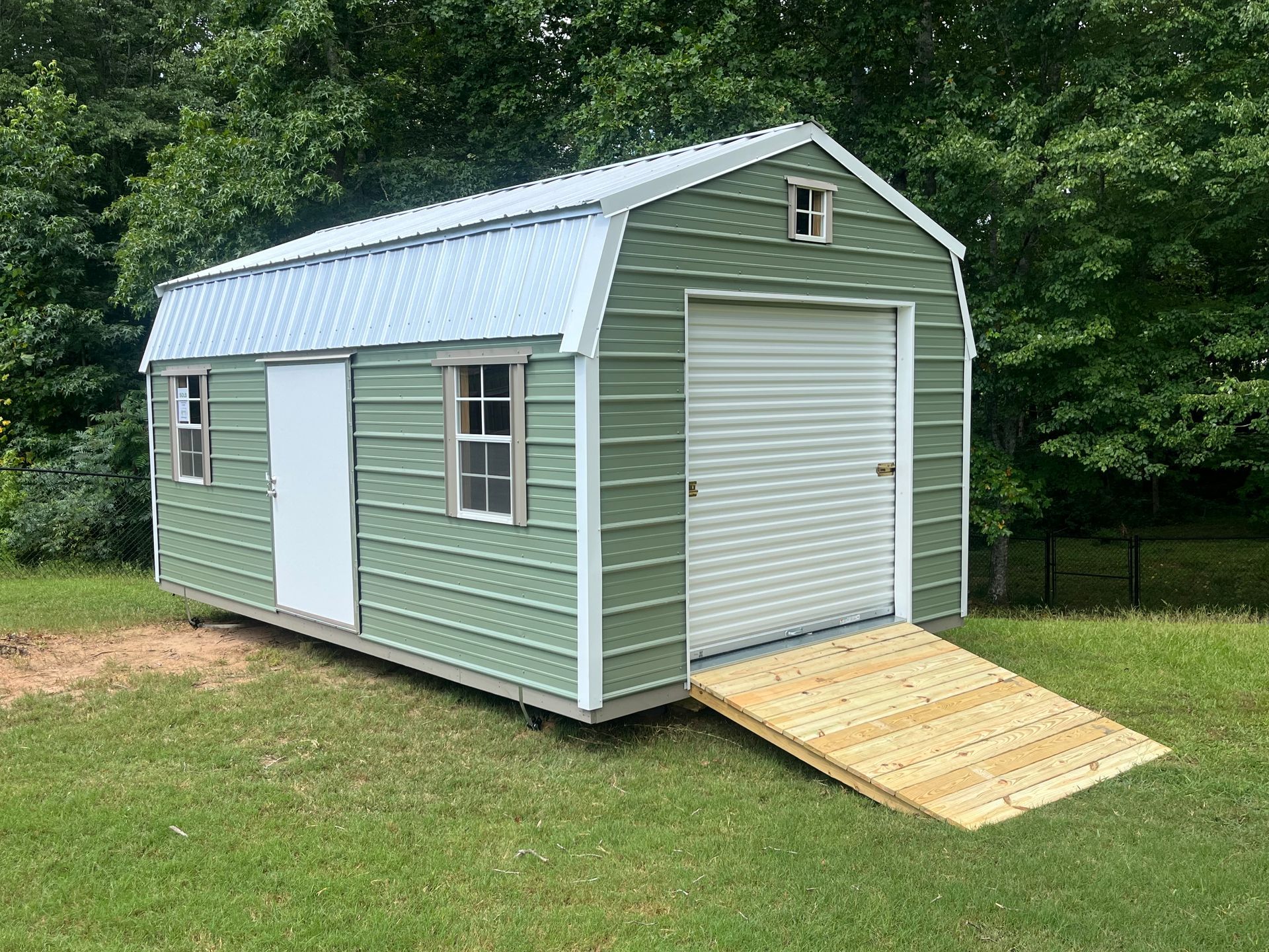 A green shed with a wooden ramp attached to it is sitting on top of a lush green field.
