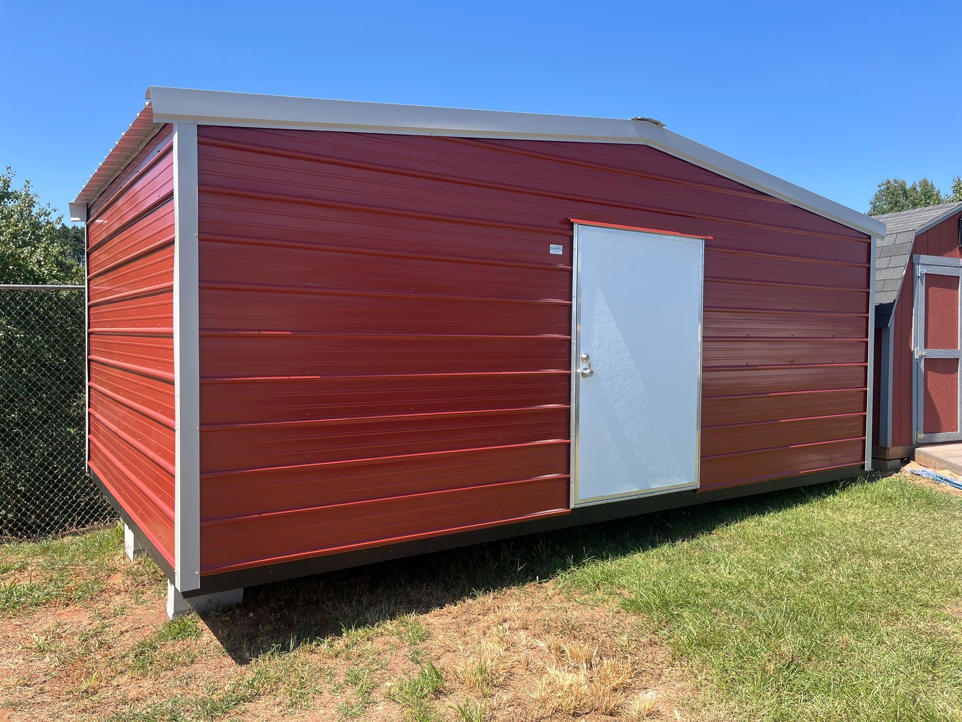 Red shed with a white door in a grassy yard on a sunny day.