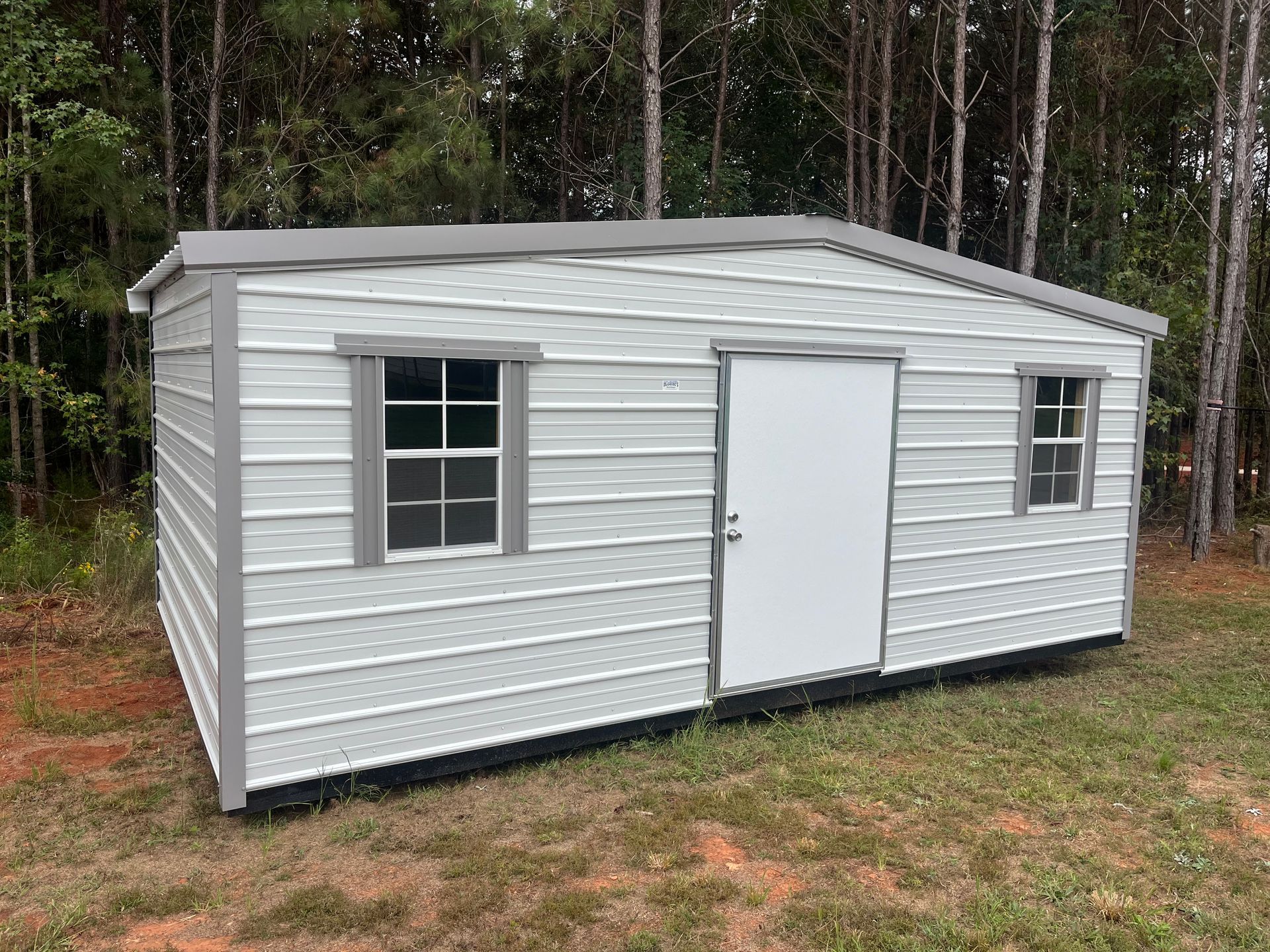Gray and white shed with a door and two windows, set in a grassy area with trees in the background.