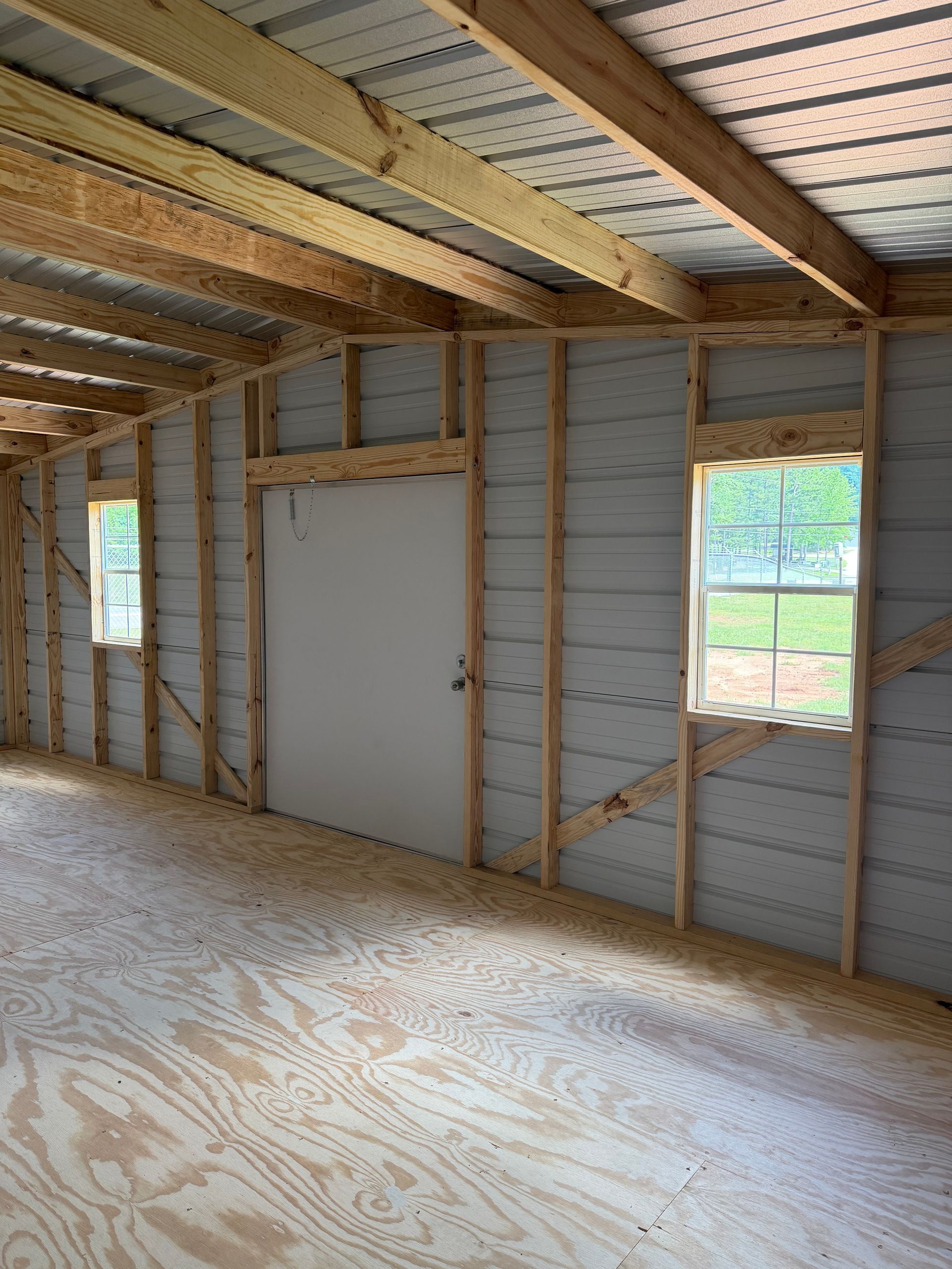 Unfinished room with exposed wood framing, insulation, plywood floor, and a white door and window opening.