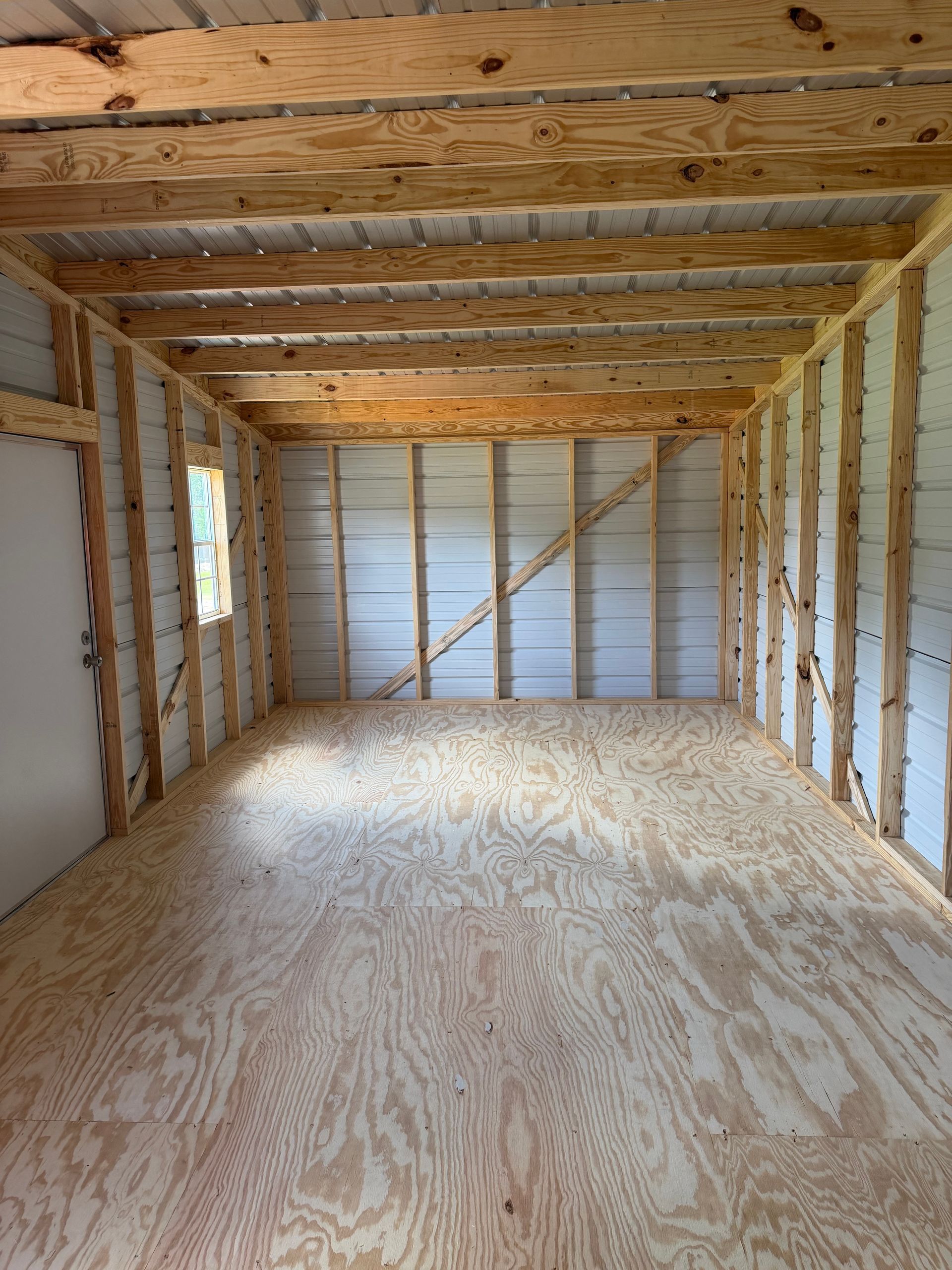 Empty wooden shed interior with exposed framing, plywood floor, and unfinished walls and ceiling.
