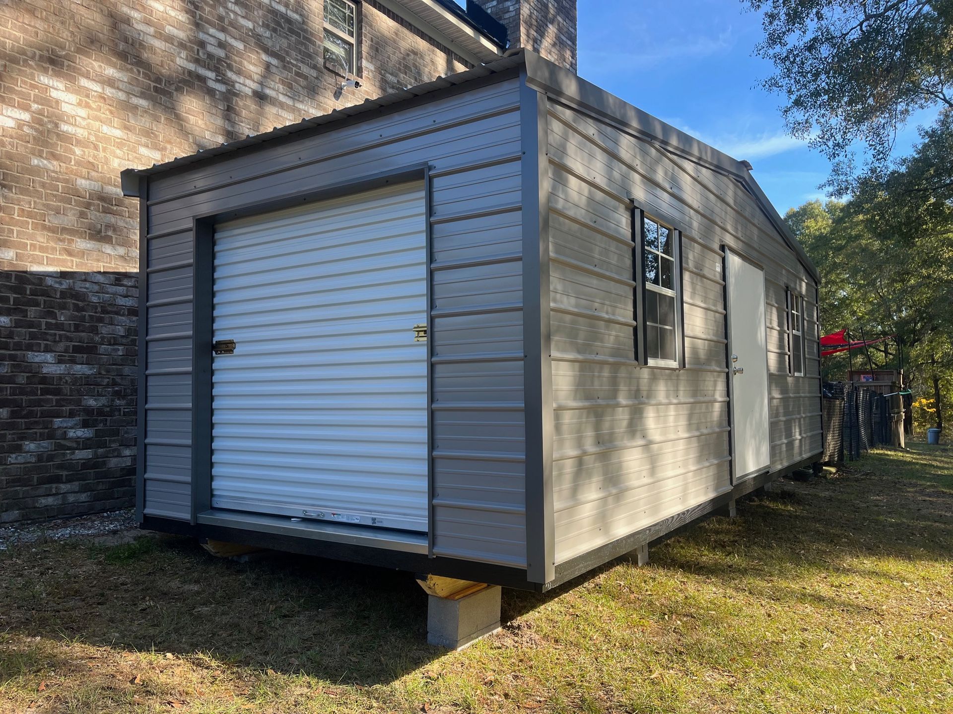 Gray shed with a roll-up garage door, small window, and a door, set in a grassy yard.