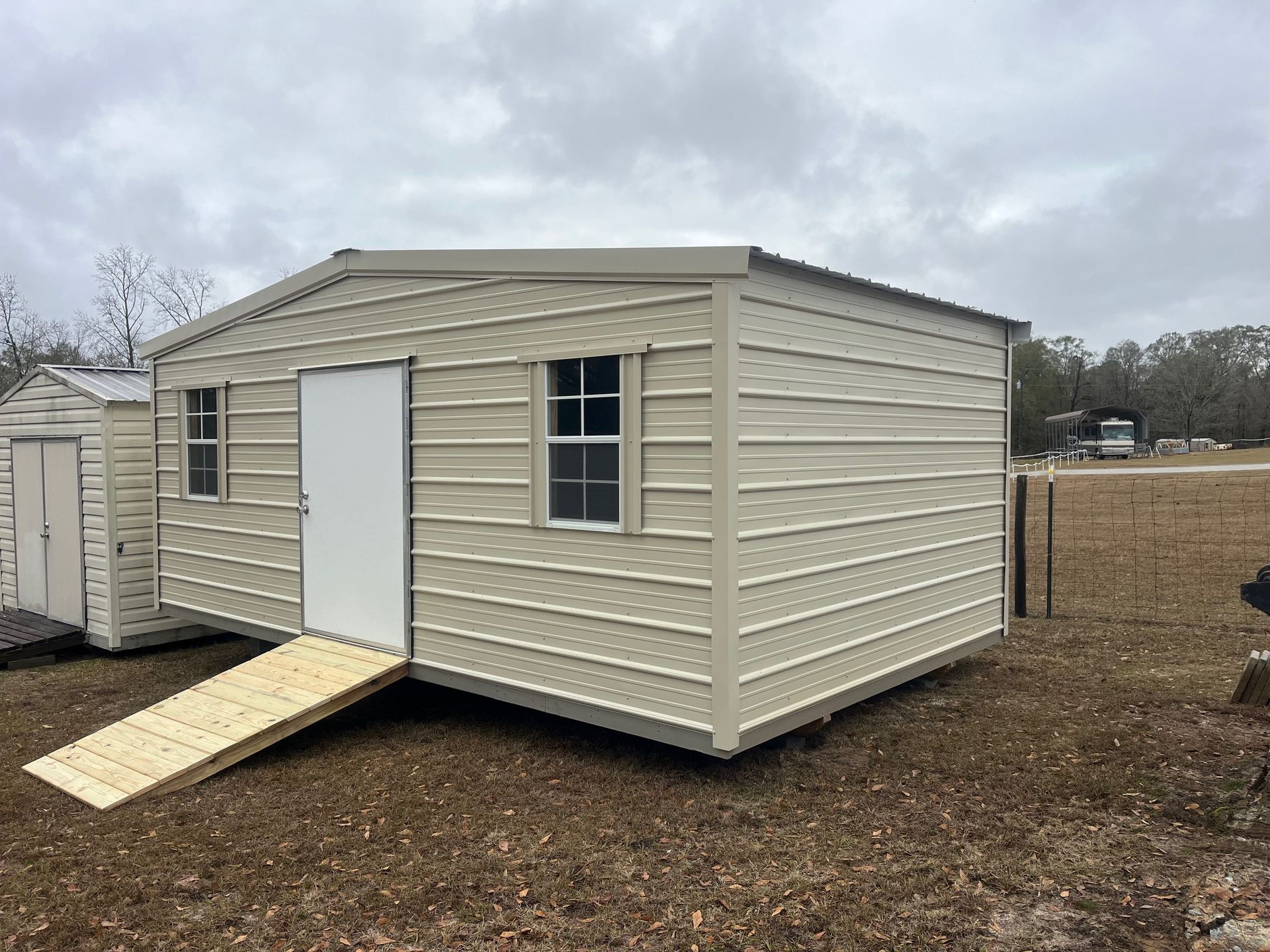 Tan metal shed with a white door and ramp, windows, outdoors.