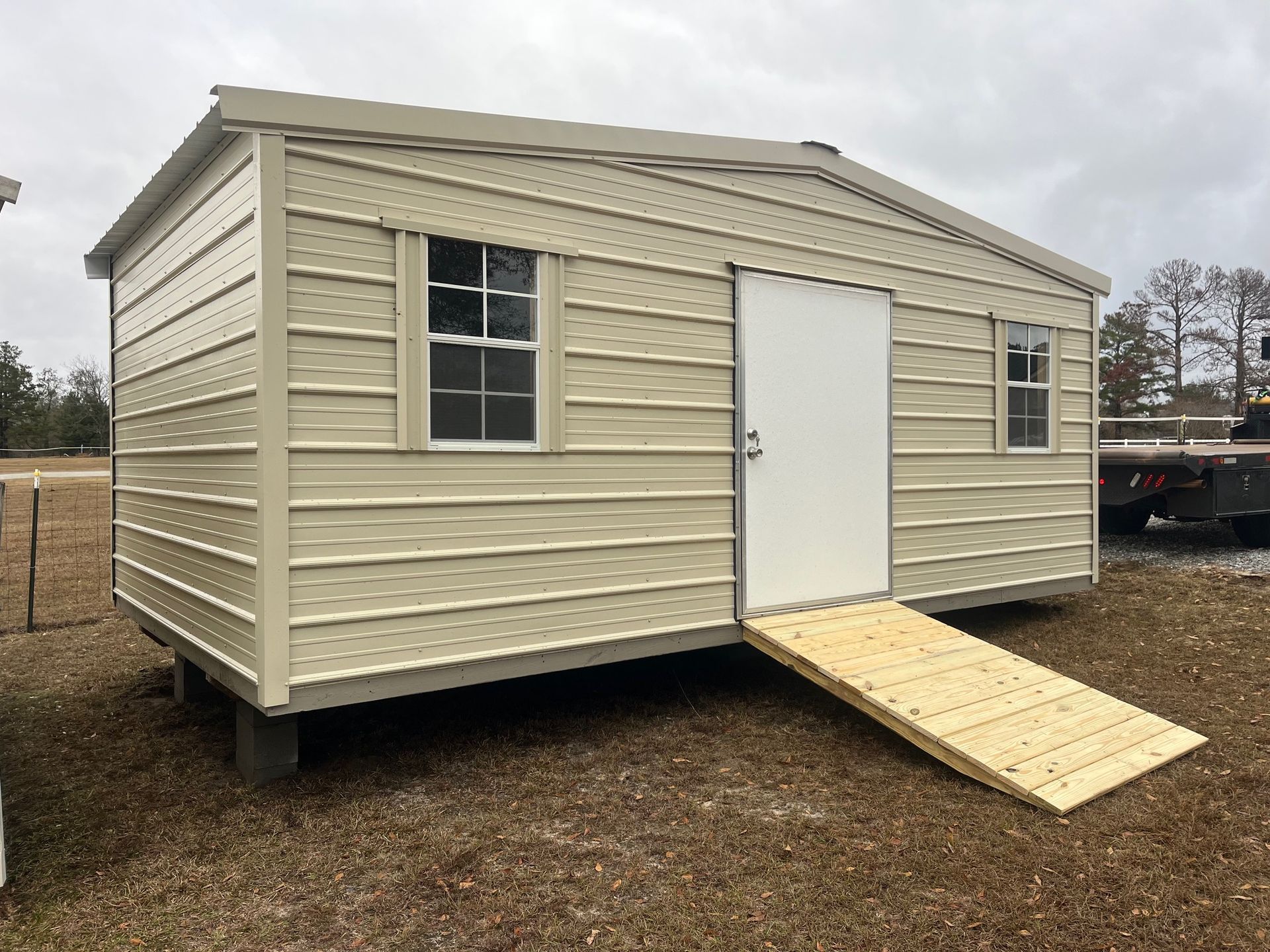 Tan metal shed with a ramp and two windows.