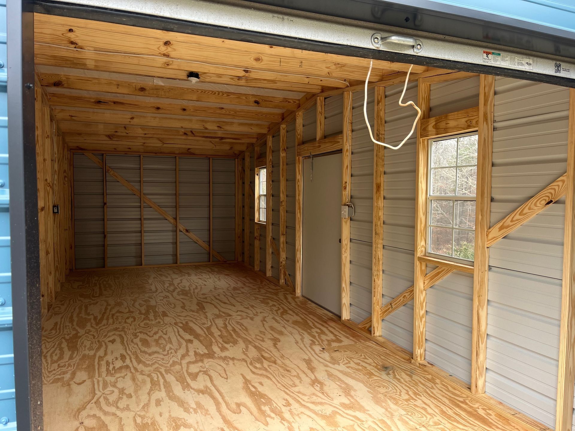 Interior of a wooden-framed shed, with a plywood floor and ceiling. There are metal walls and two windows.