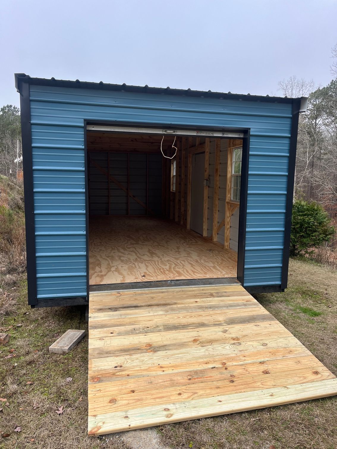 Blue metal shed with a wooden ramp, open door.