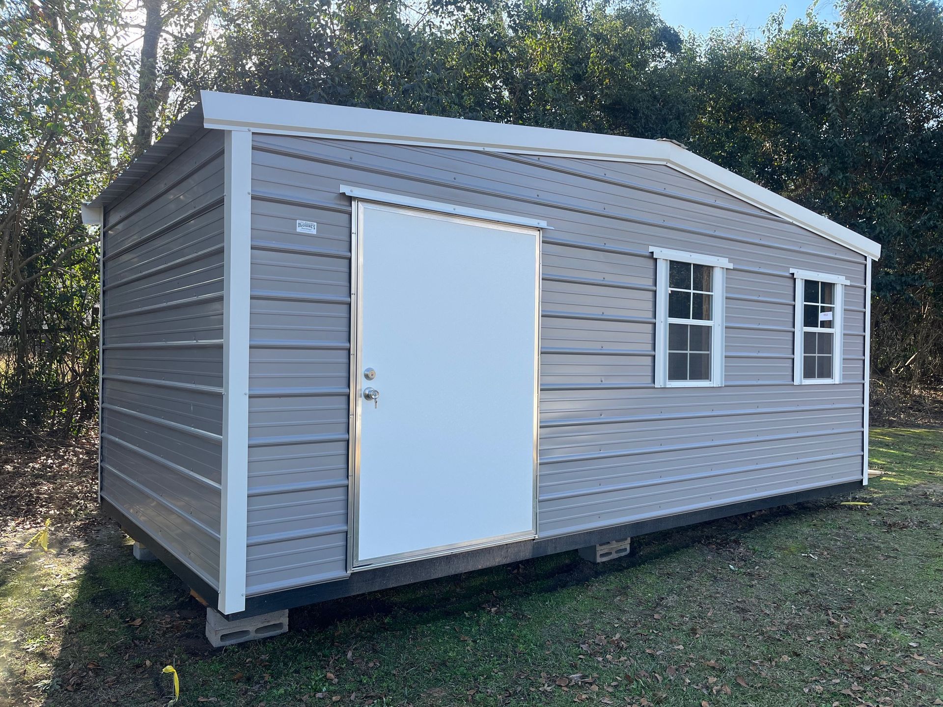 Gray shed with white trim, door, and windows, on a grassy plot.