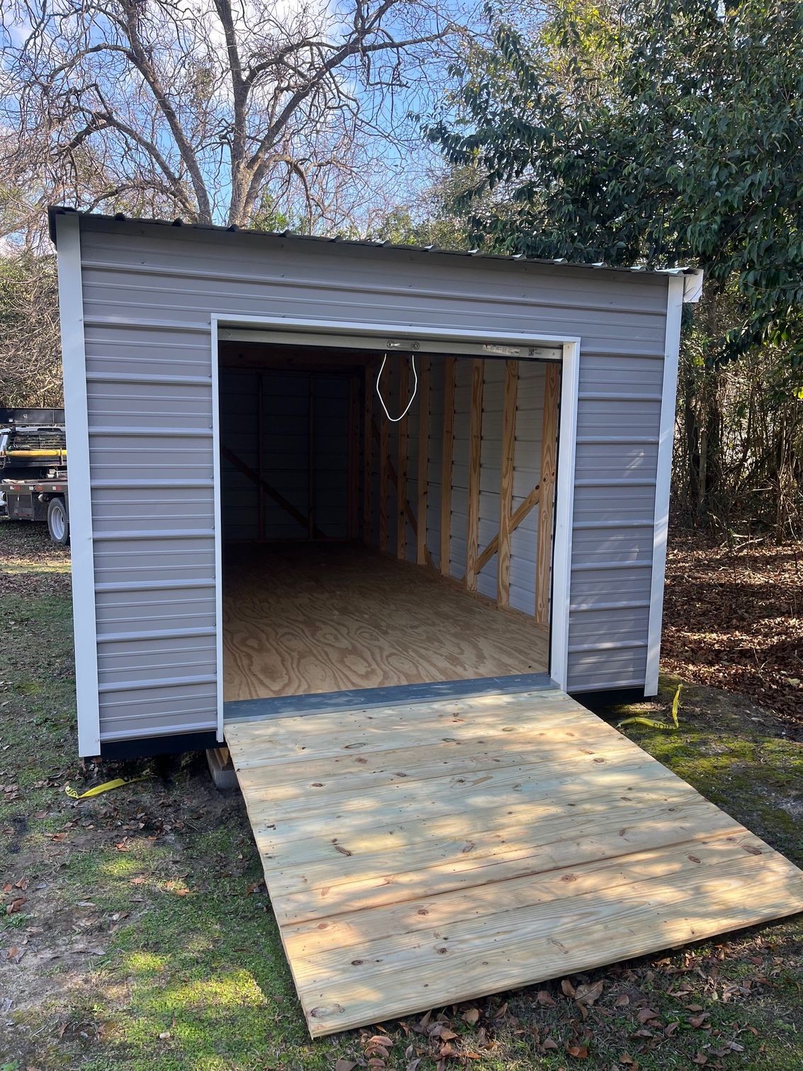 Gray shed with an open door and wooden ramp outdoors.
