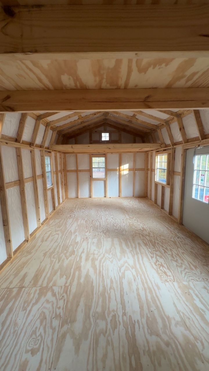 Interior of an unfinished shed with plywood floor, walls, and ceiling. Windows and rafters visible.