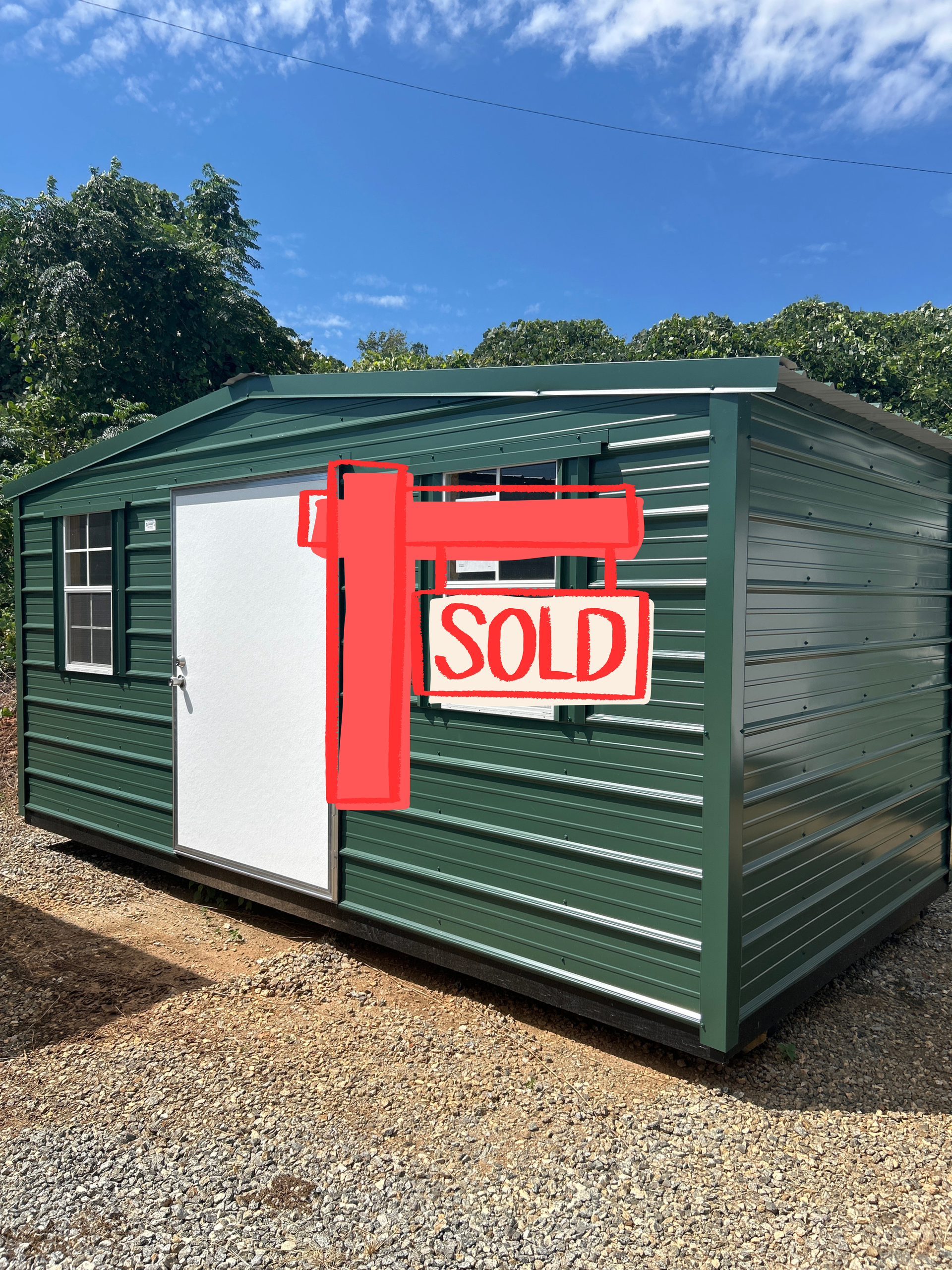 Green metal shed with a white door and windows under a blue sky.