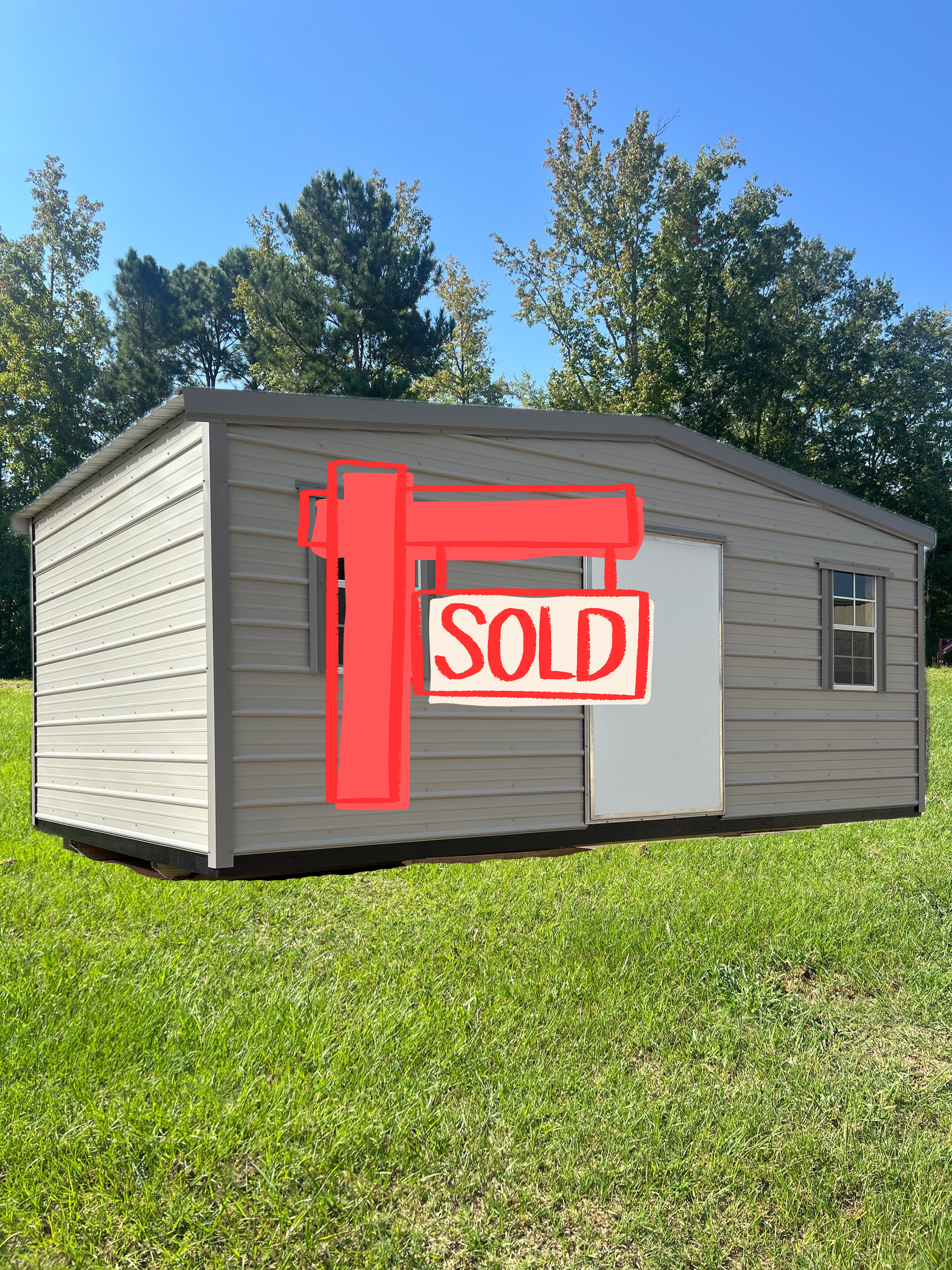 Light gray storage shed with a white door and two windows sitting on a grassy lawn under a clear blue sky.