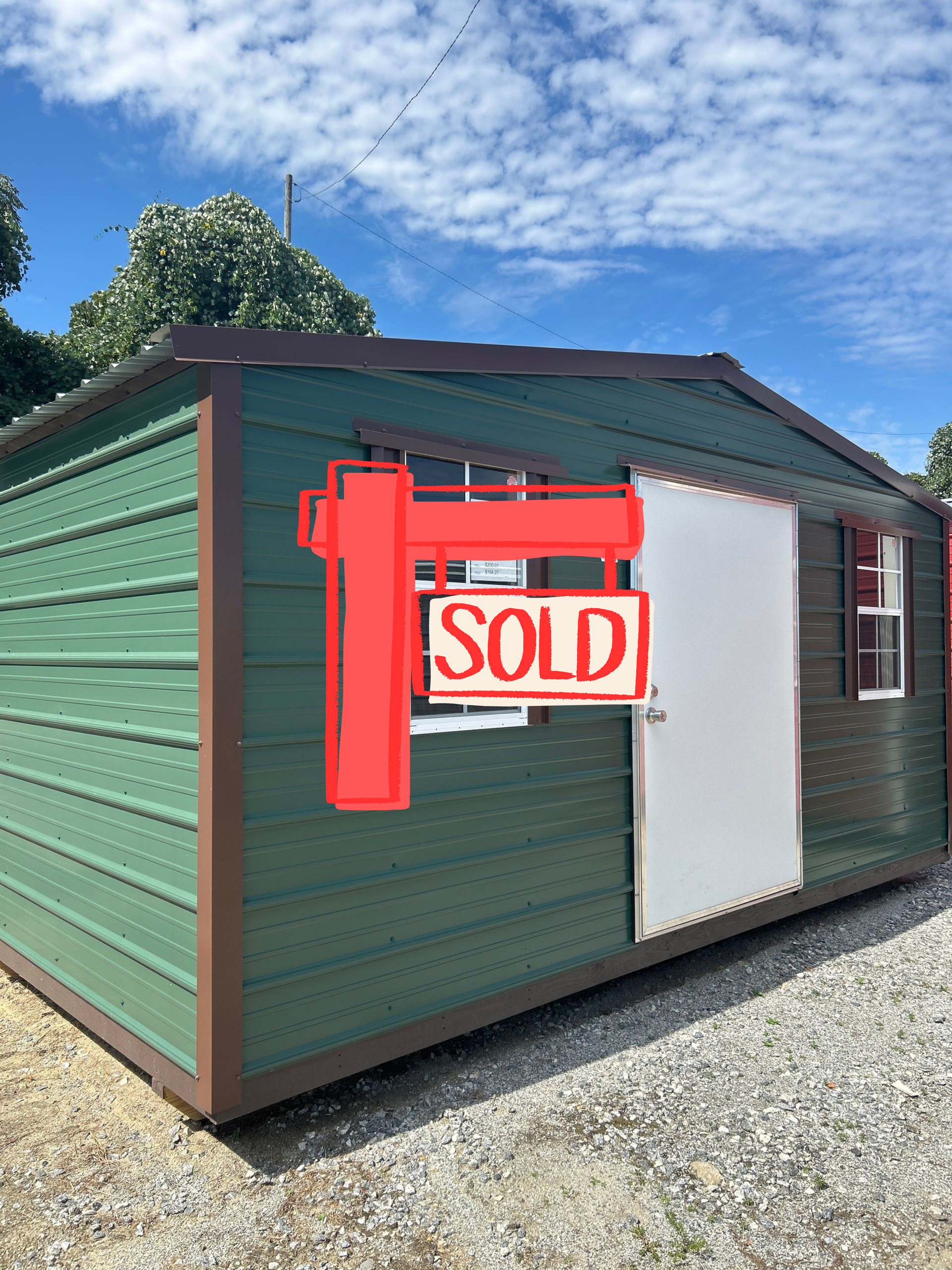 Green storage shed with brown trim, white door, and two windows, set outdoors under a blue sky.