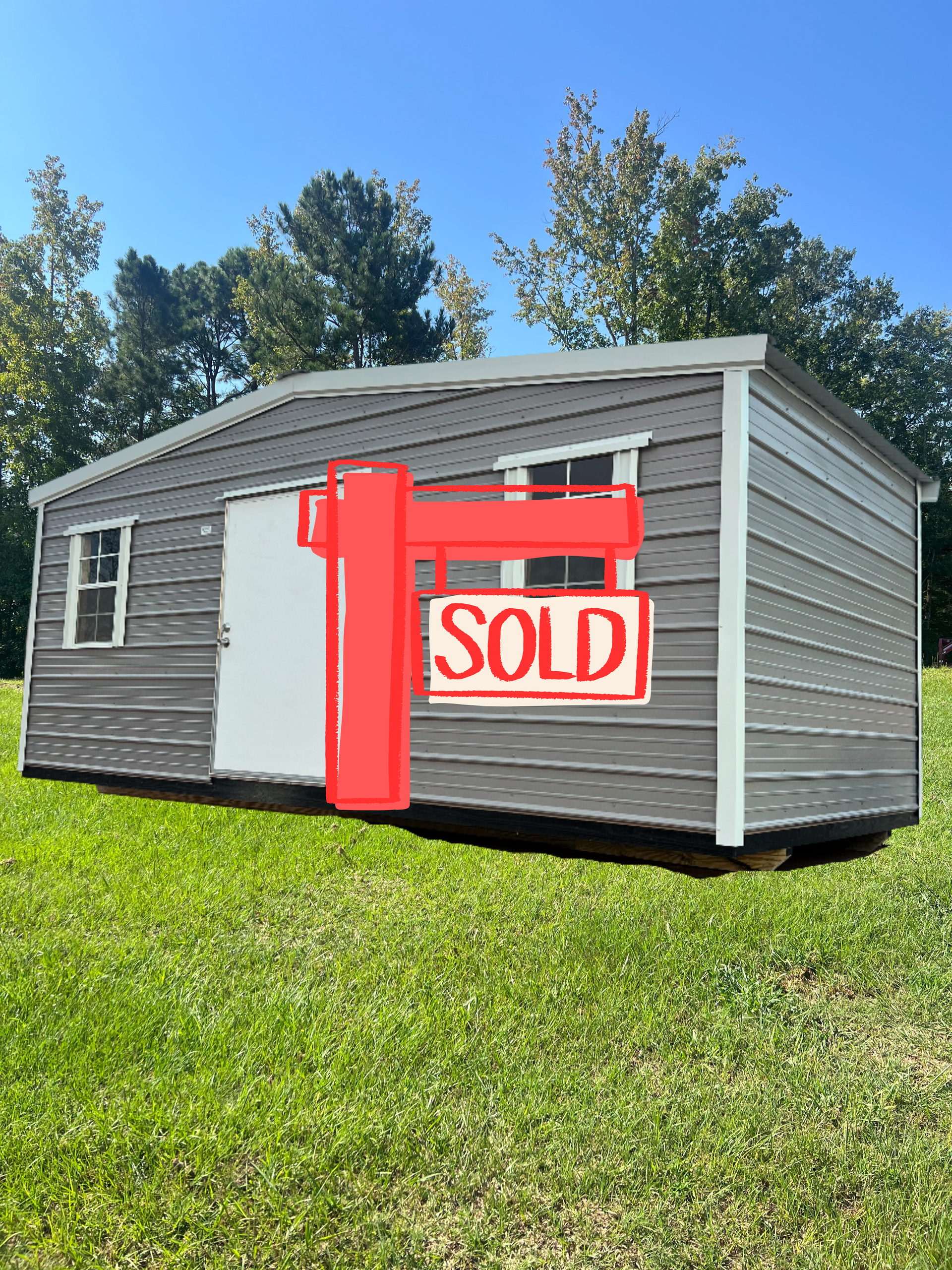 Gray shed with white trim, door, and windows, on green grass under blue sky.