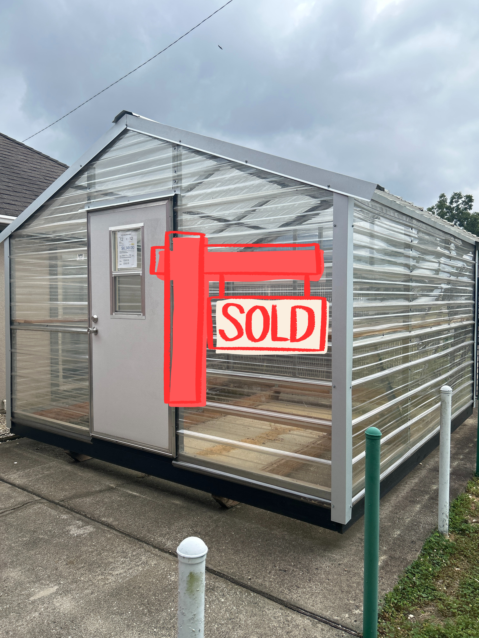 Greenhouse with clear corrugated plastic walls, white frame, and a door, set on a concrete pad.