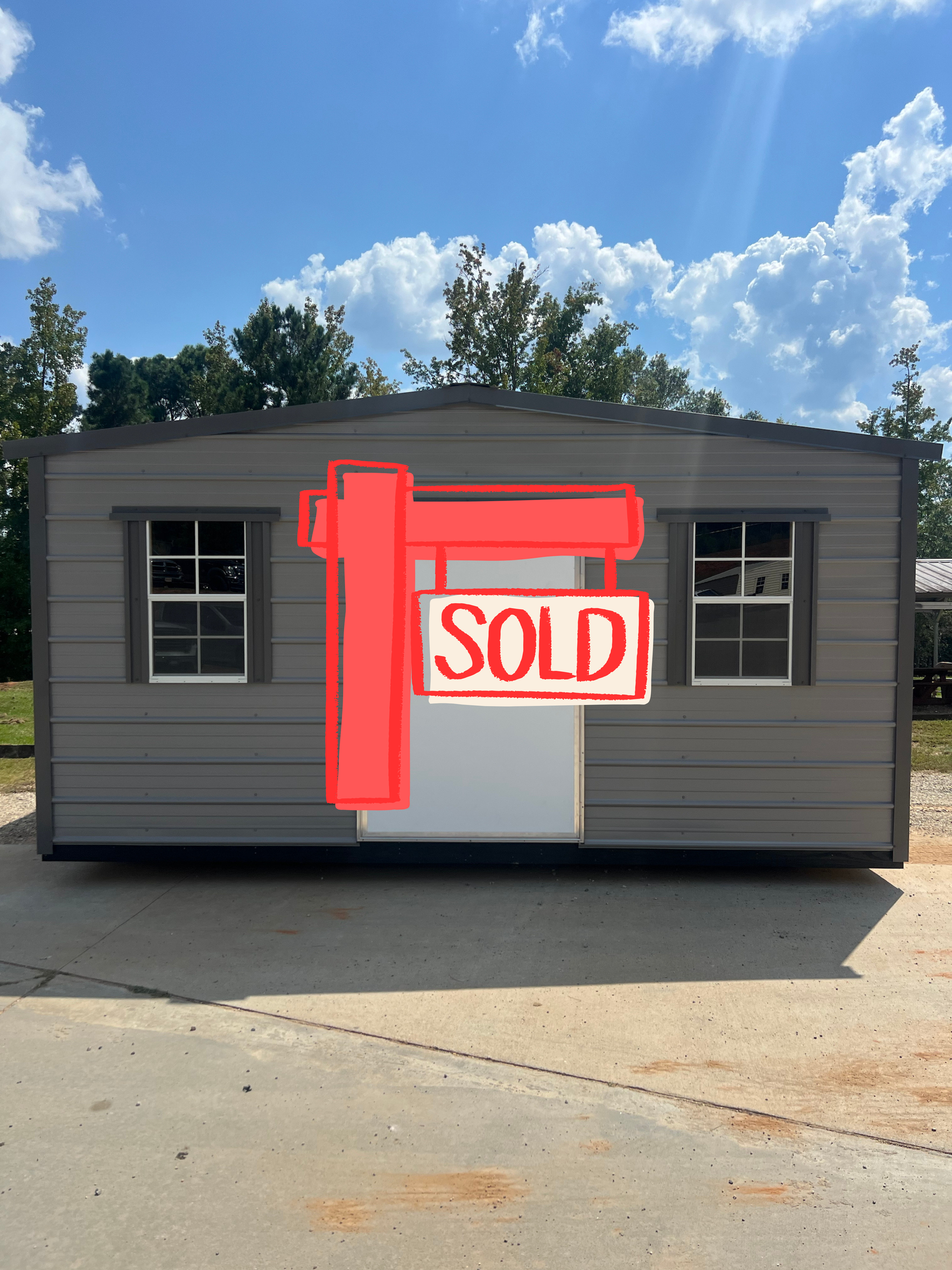 Gray shed with white door and windows against a blue sky with clouds.