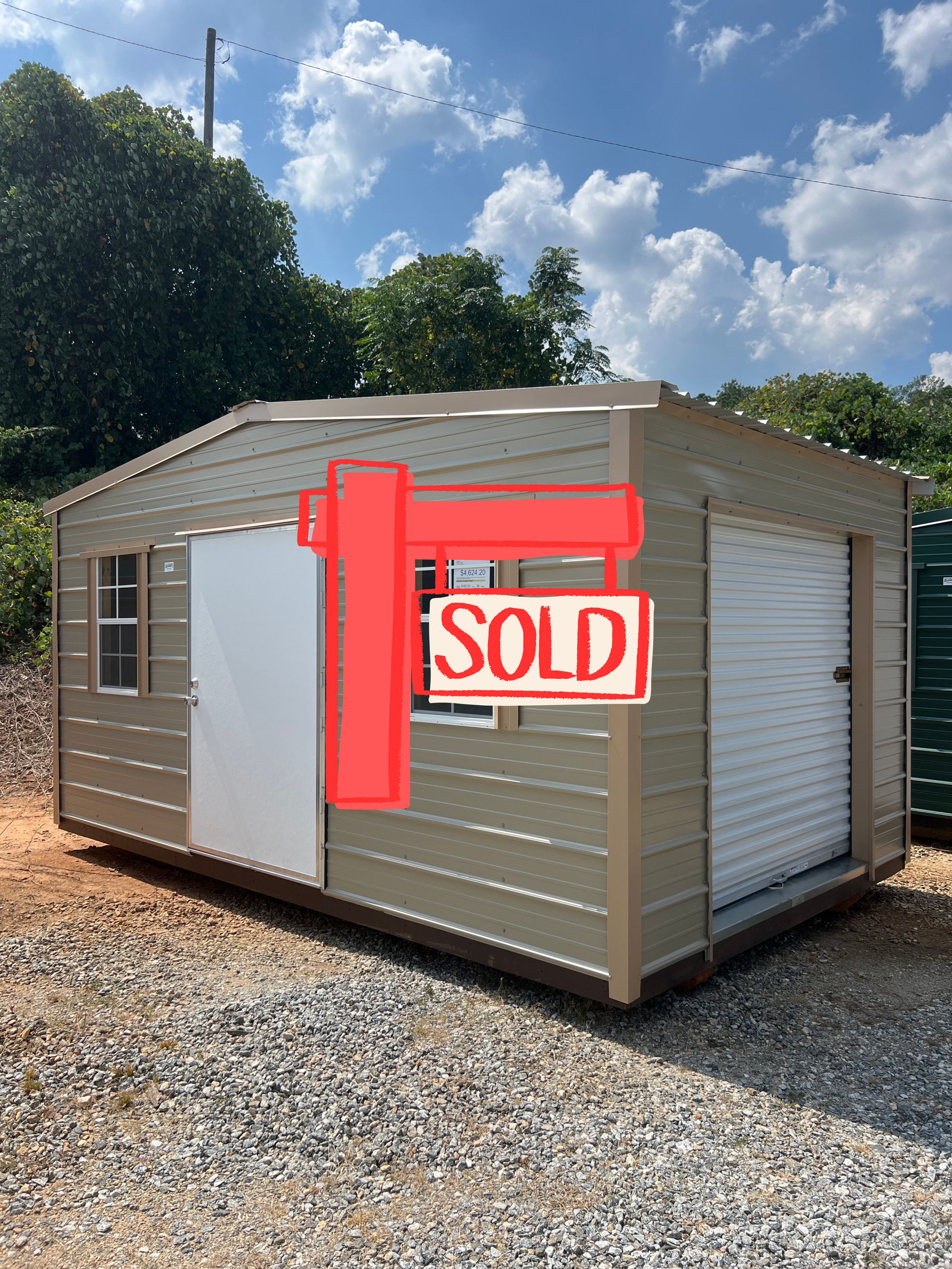 Tan shed with brown trim, SOLD sign on the door, windows, and overcast sky.