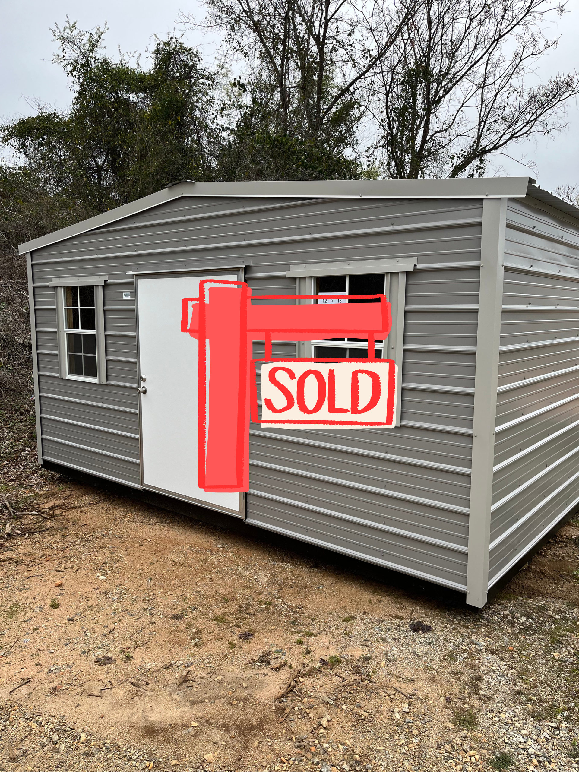 Gray metal shed with a white door and two windows, outdoors.