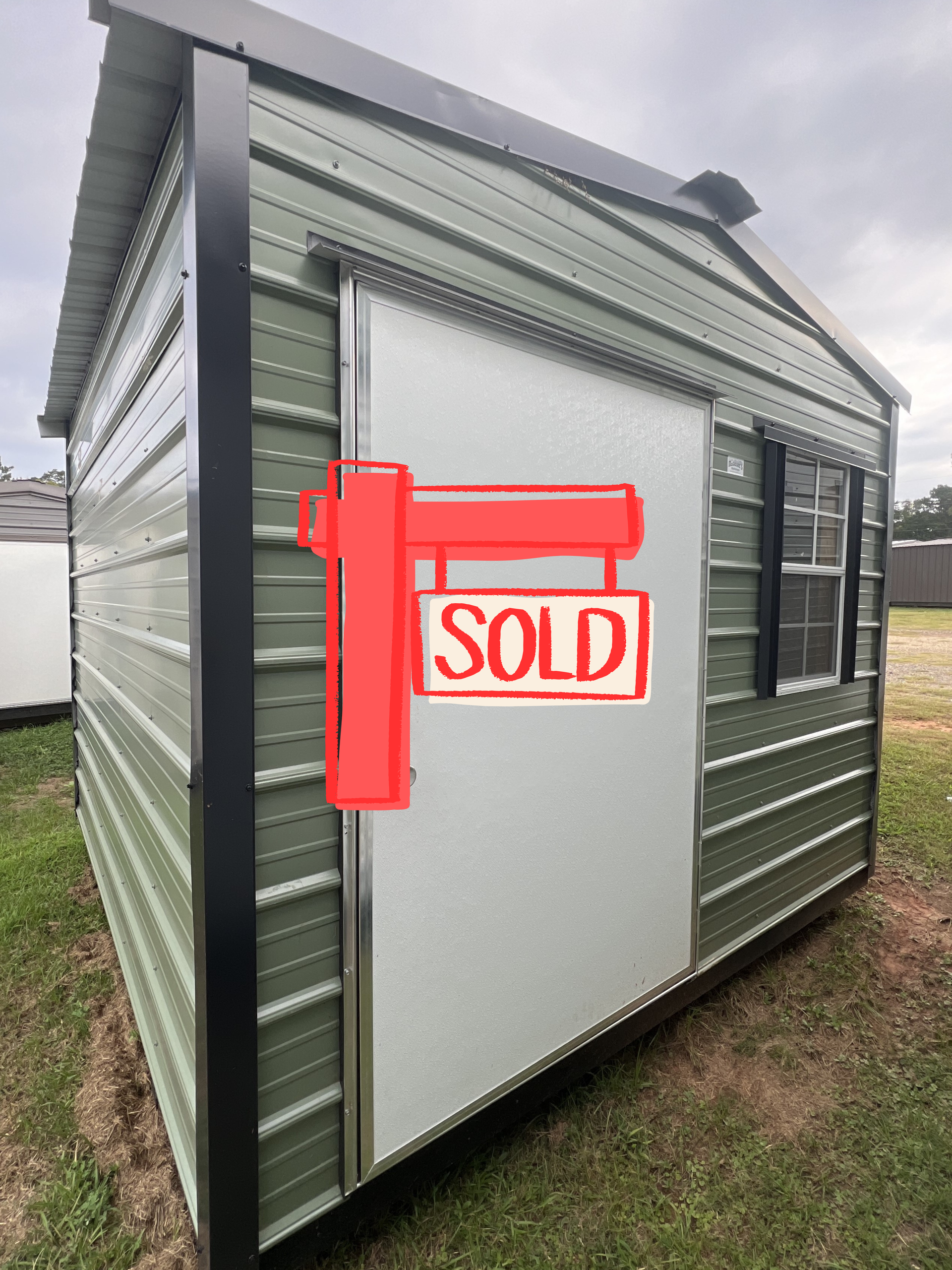 Green metal storage shed with white door and small window on grass.