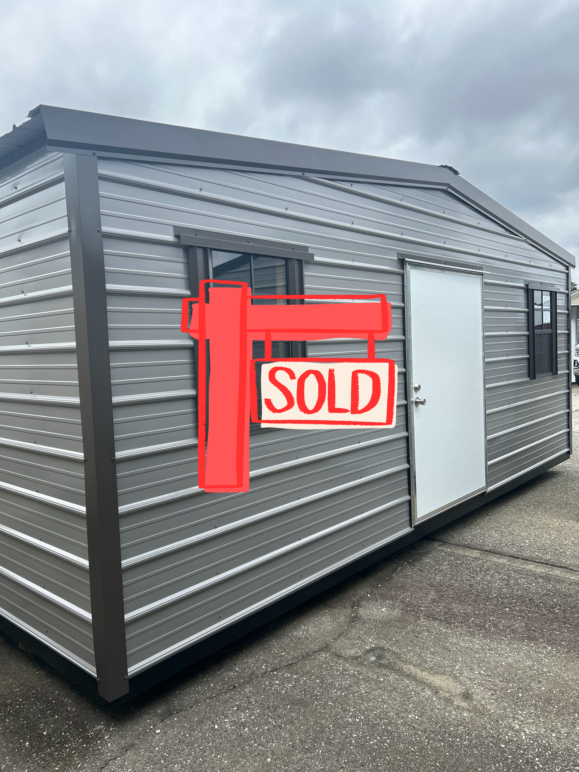Gray metal shed with a brown trim, white door, and two windows.