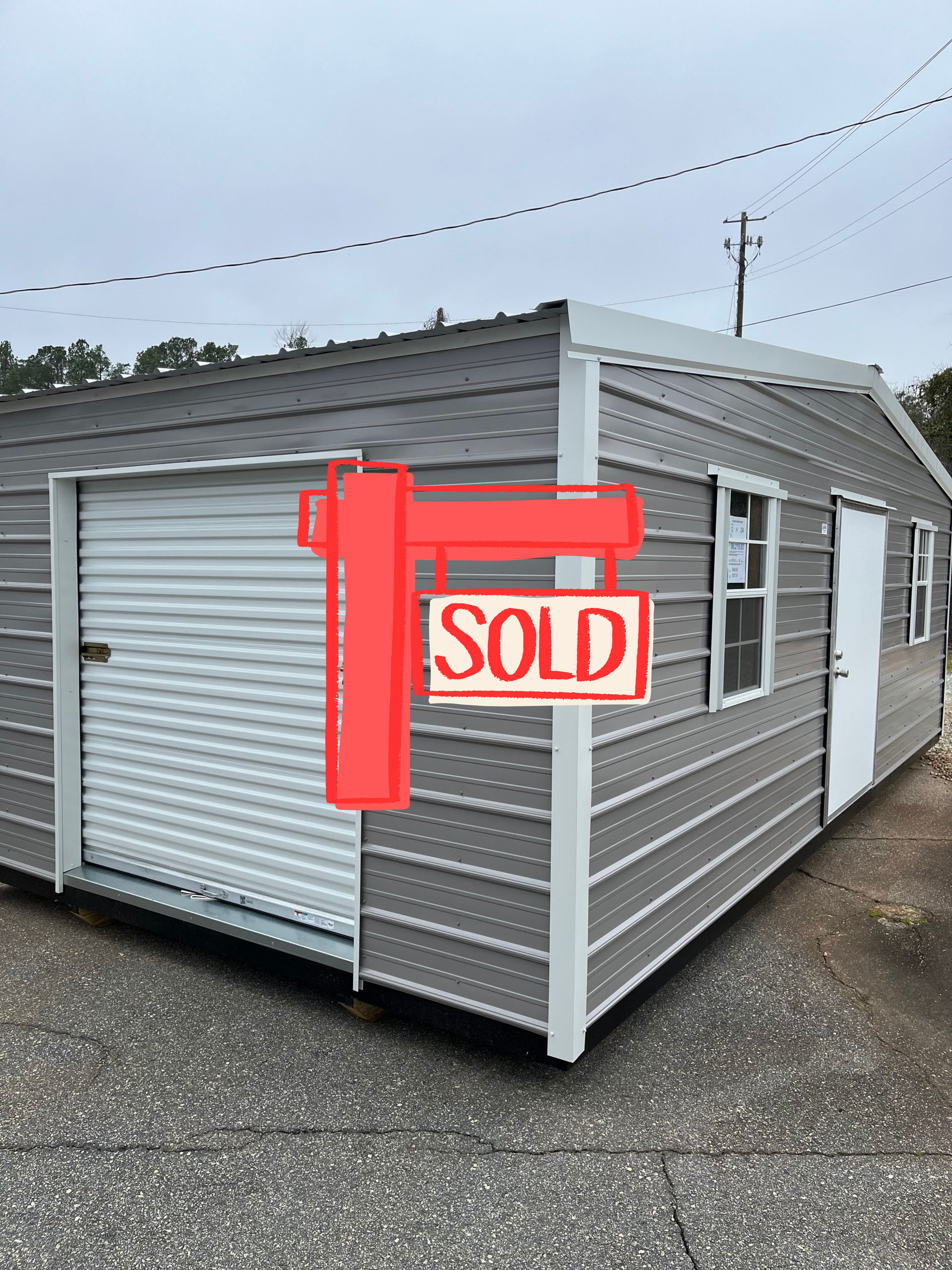 Gray metal shed with a roll-up door, a window, and a white door, on a gray pavement.