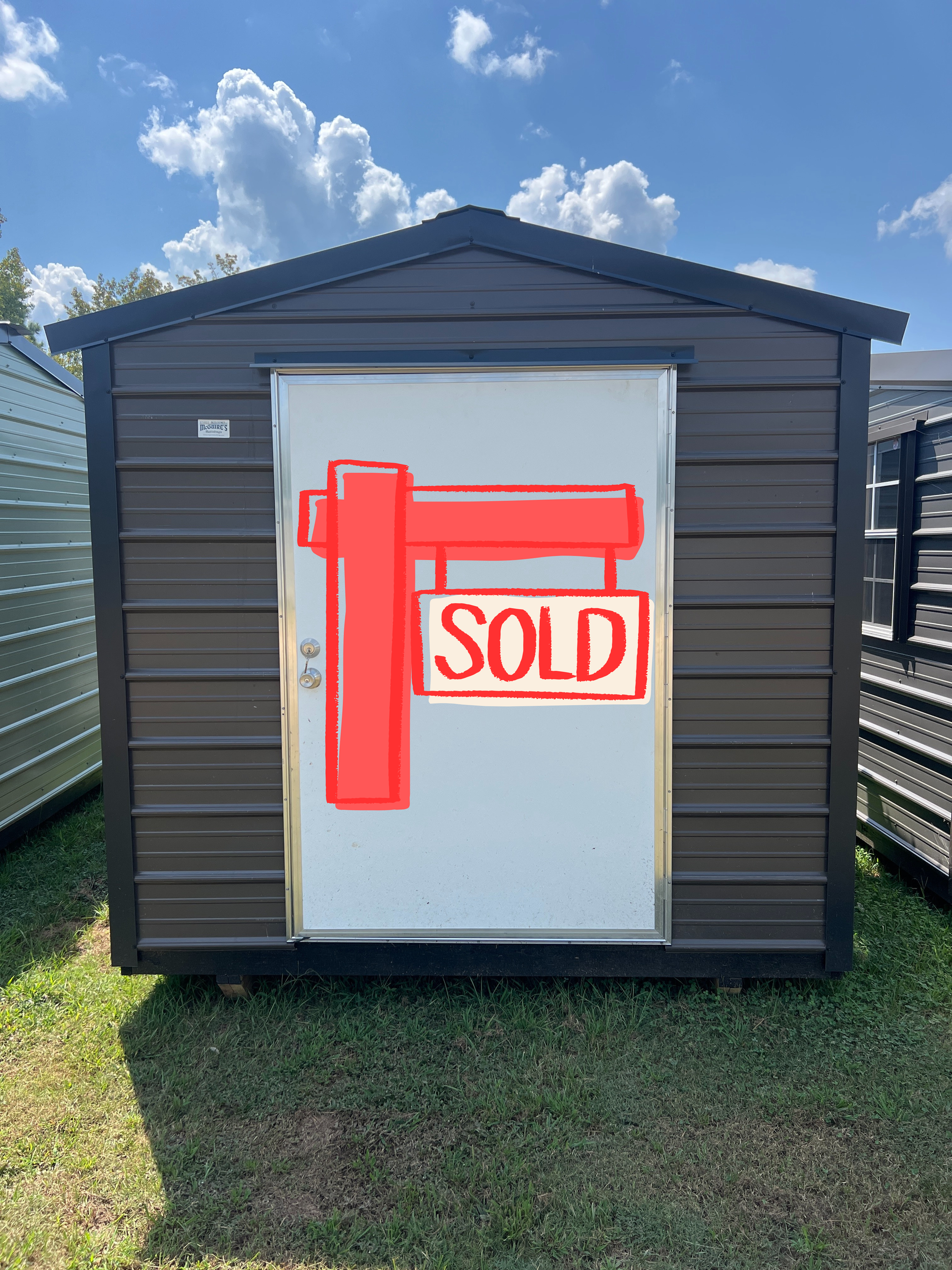 Brown metal shed with white door on green grass under blue sky.