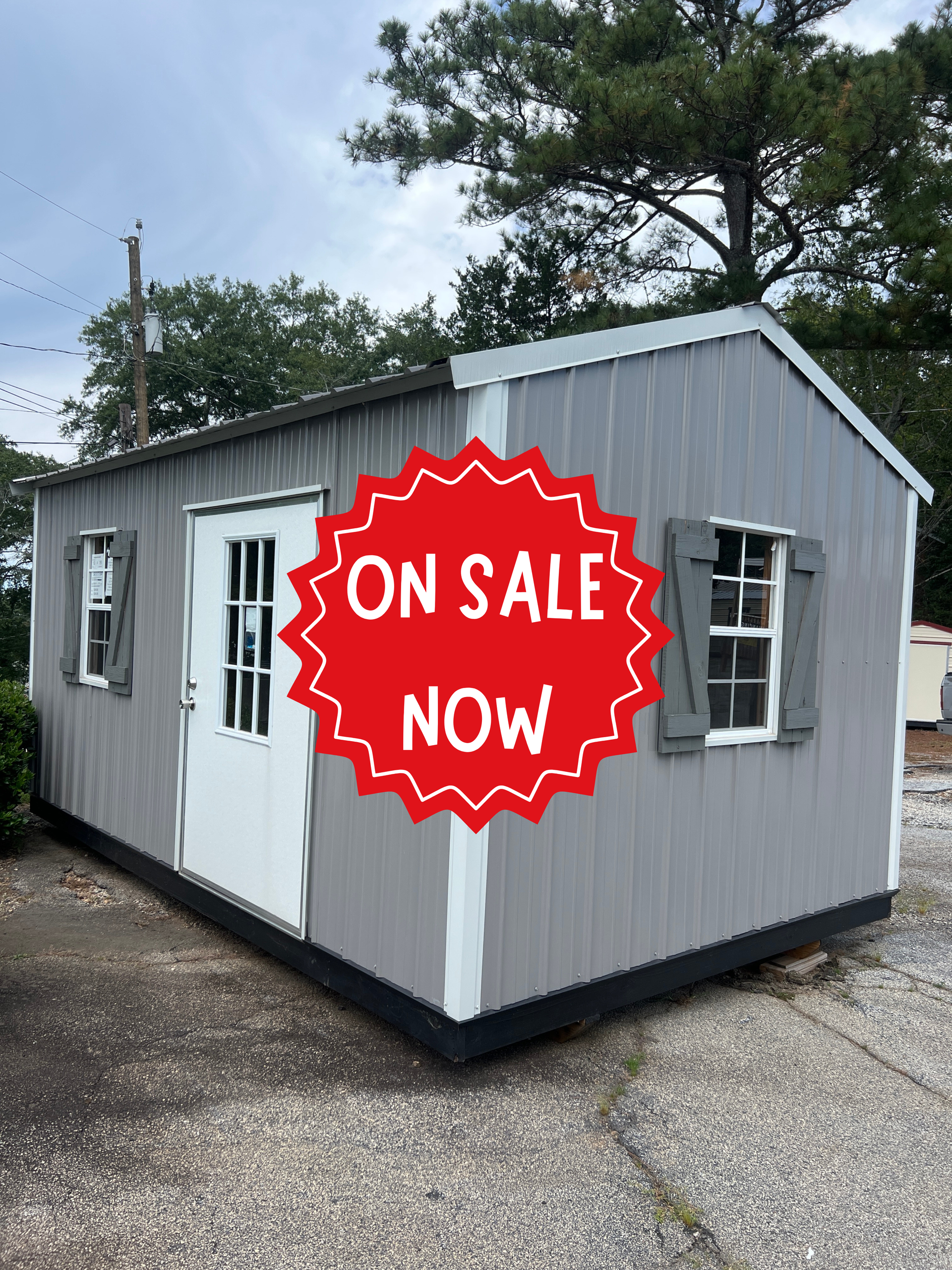 Gray portable building with white trim and a red “On Sale Now” sign outdoors