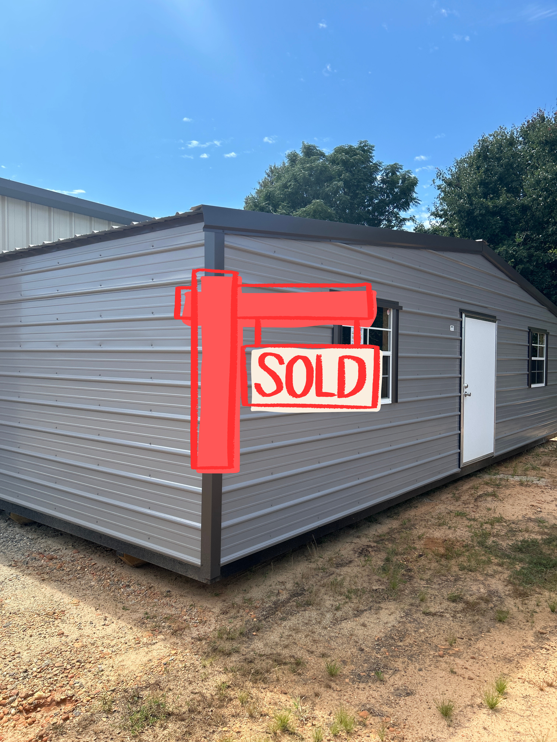 Gray metal building with a red sold sign on the front corner under a blue sky